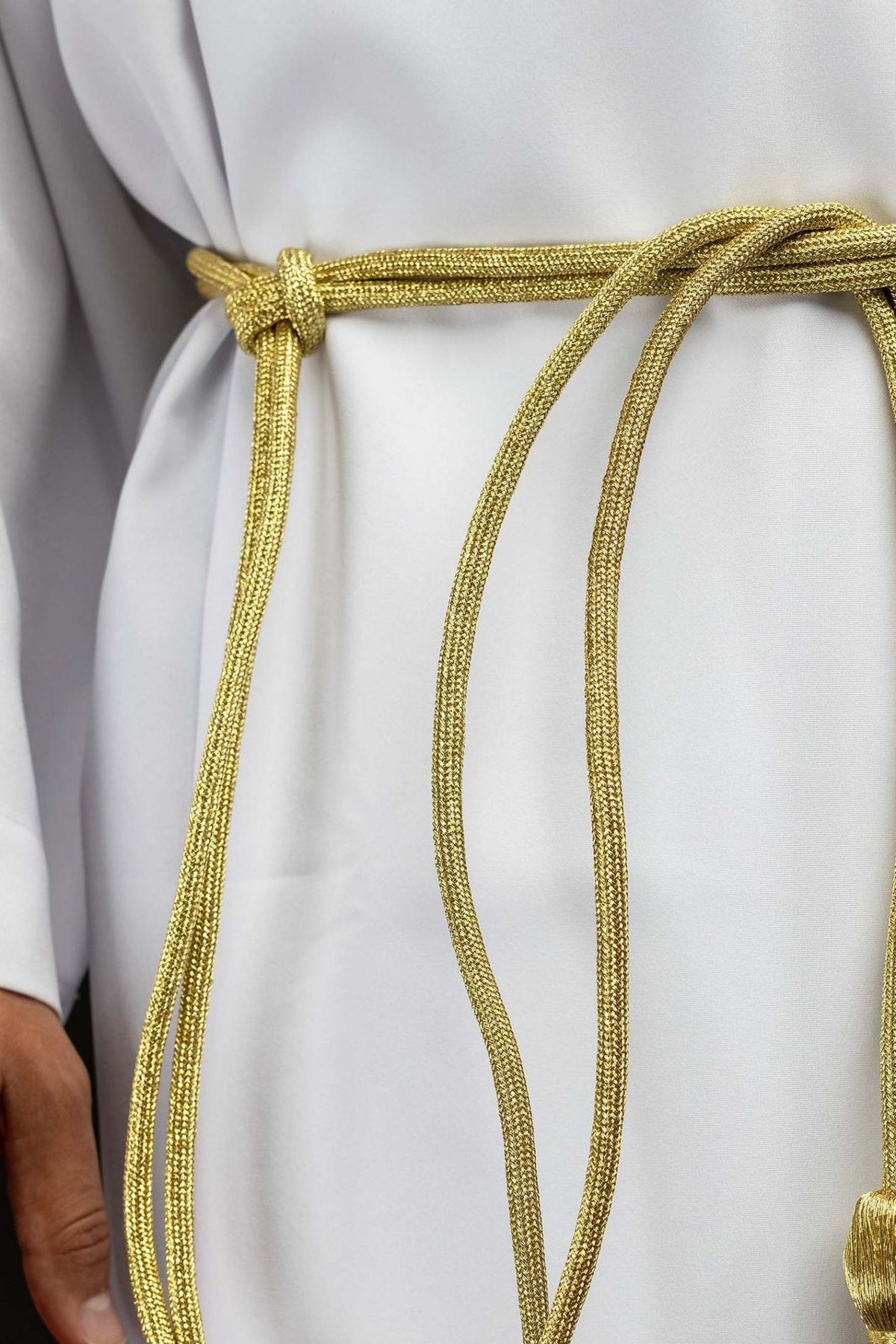 Cíngulo litúrgico dourado em close-up, mostrando o nó e o cordão trançado
