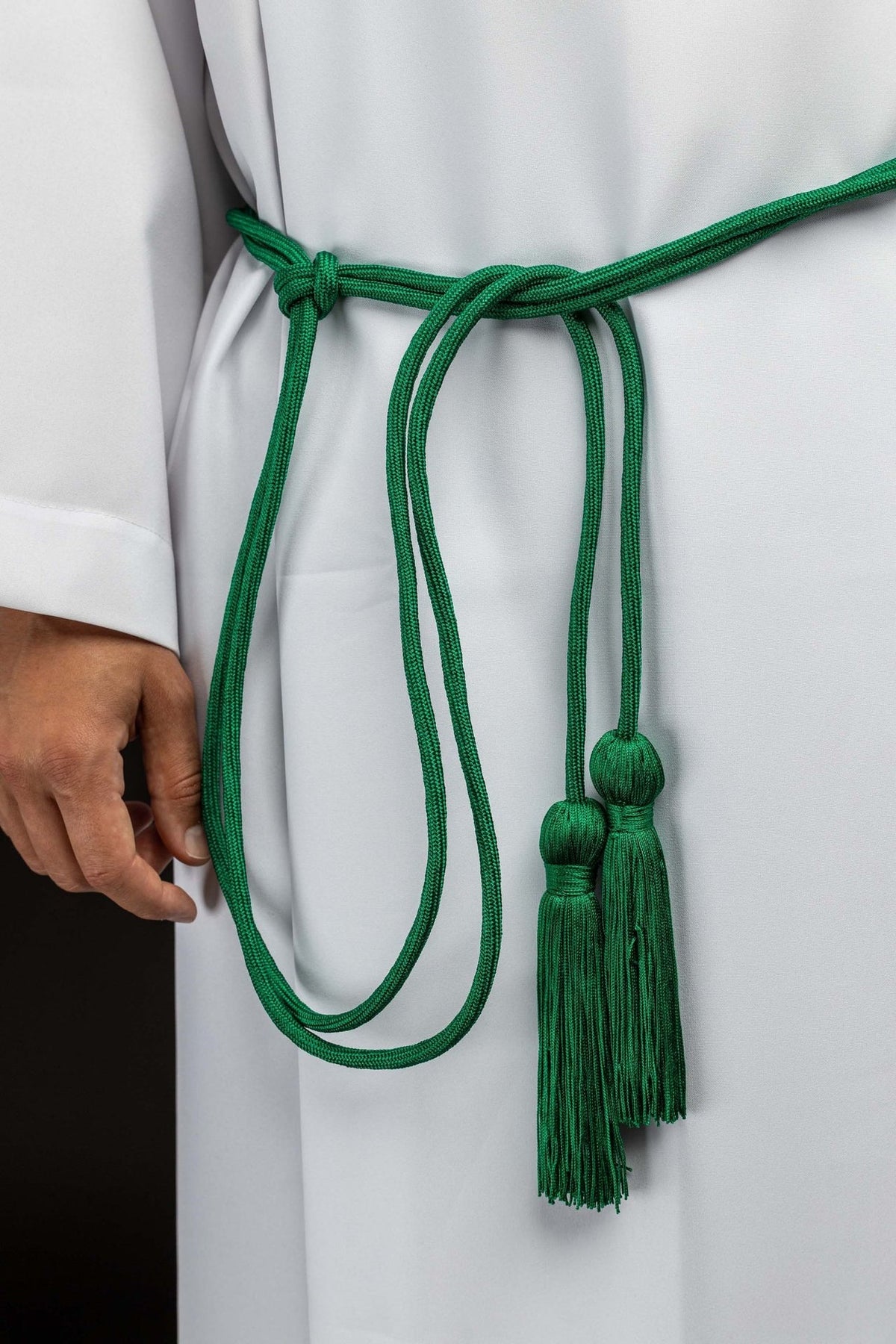 Cíngulo litúrgico verde com borlas decorativas, visto preso à alva, com cordões e duas borlas