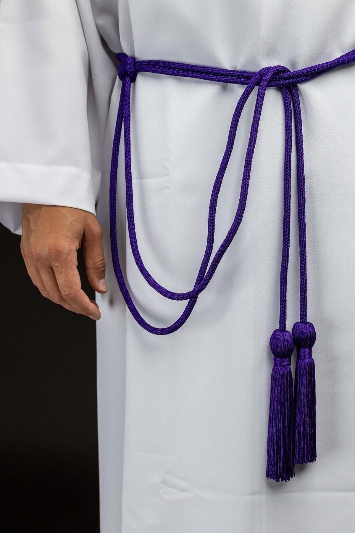 Cíngulo litúrgico roxo com borlas decorativas usado sobre alva, visto de frente