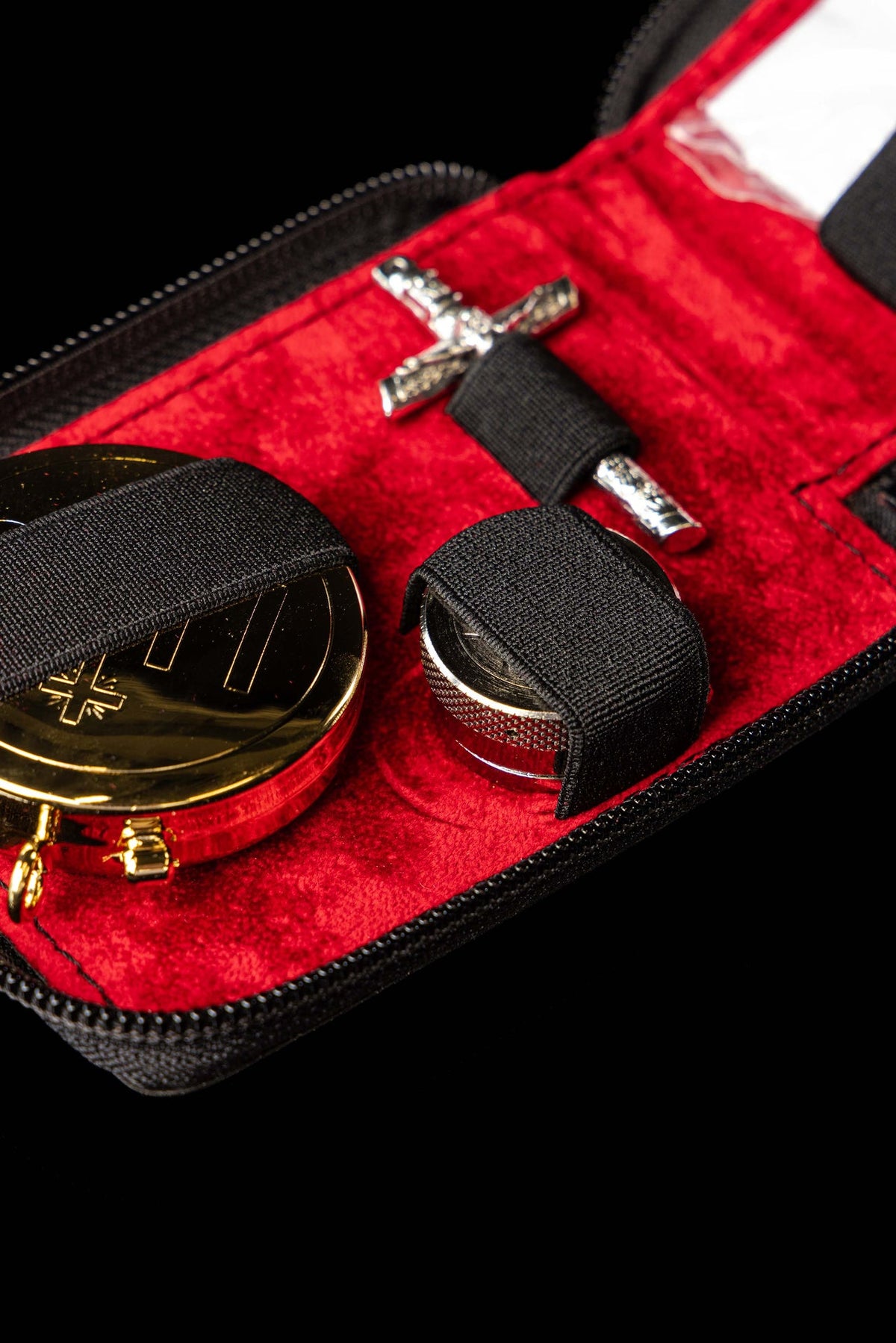 Bolsa litúrgica aberta em close-up, com cálice, patena e crucifixo presos por faixas