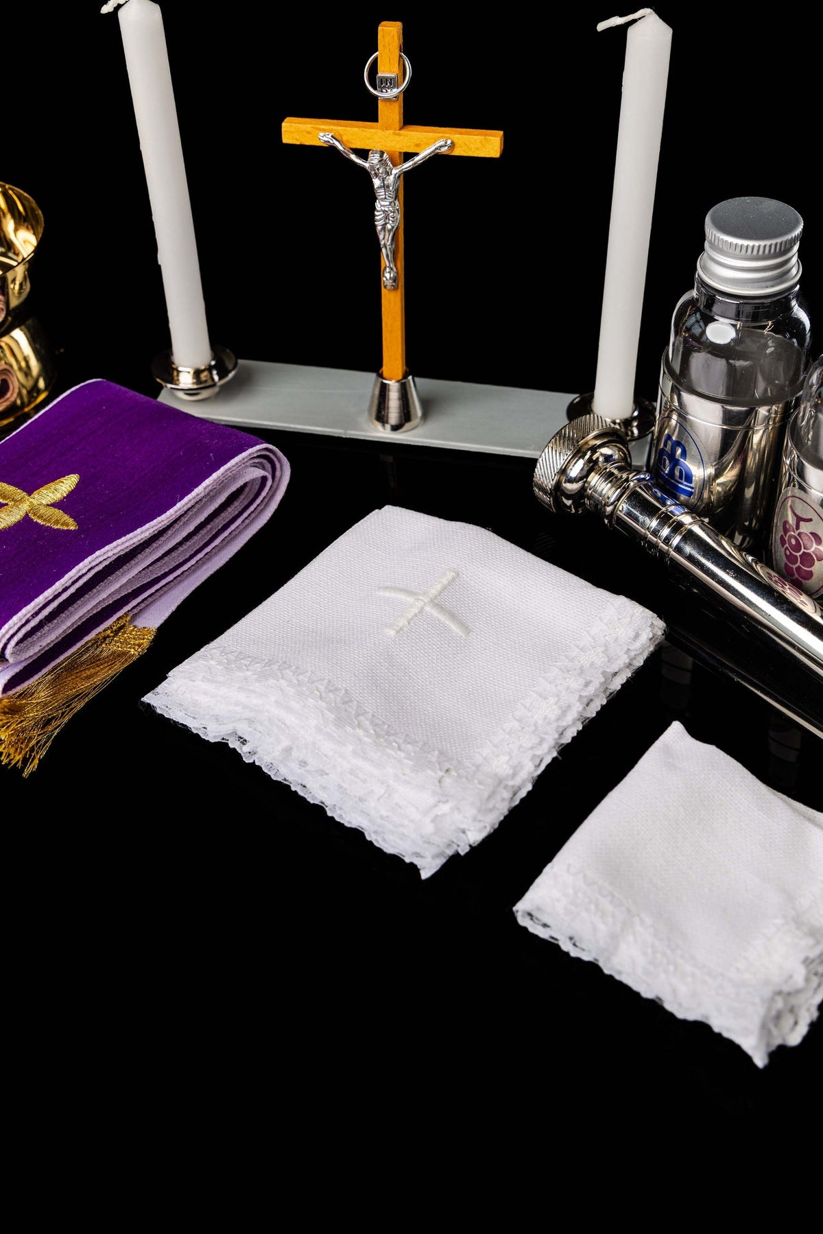 Peças da maleta litúrgica com cruz, velas, frascos e tecidos brancos