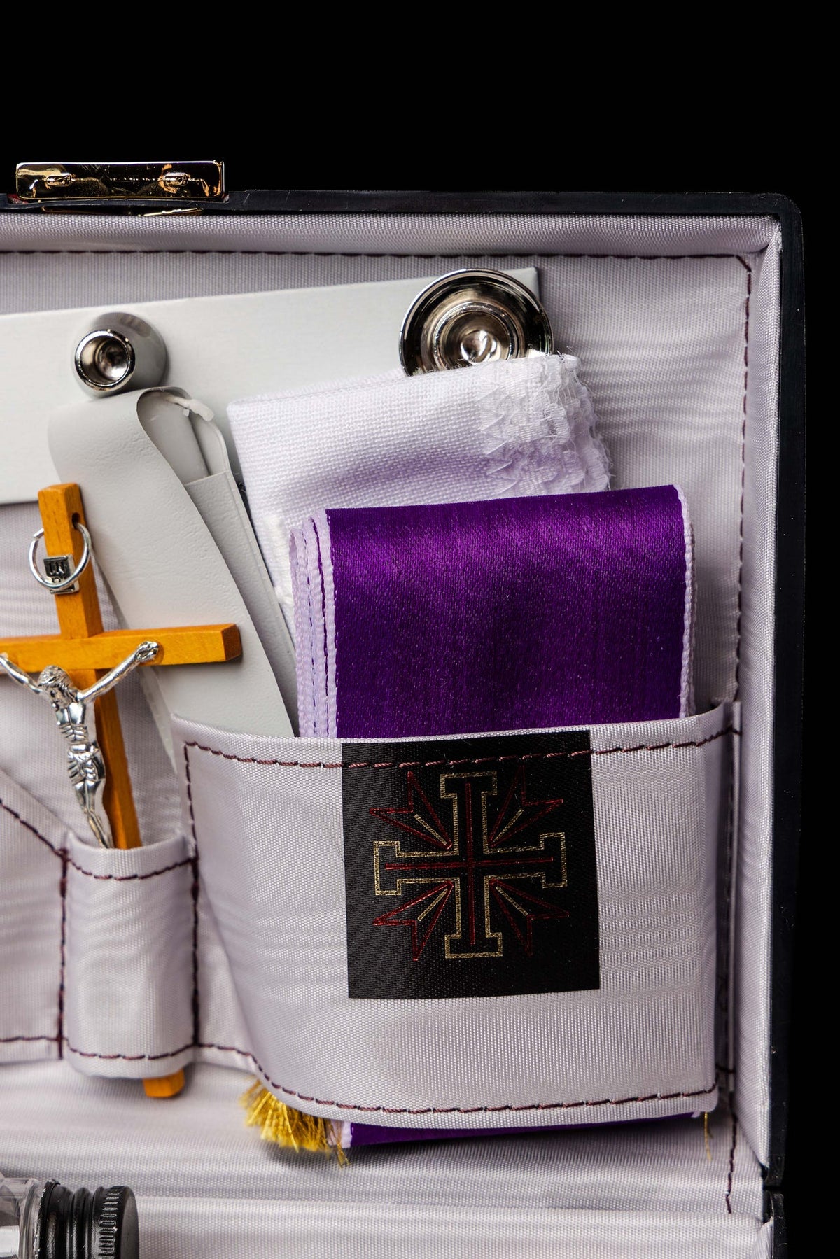 Detalhe da maleta com tecido roxo, corporal branco e cruz bordada