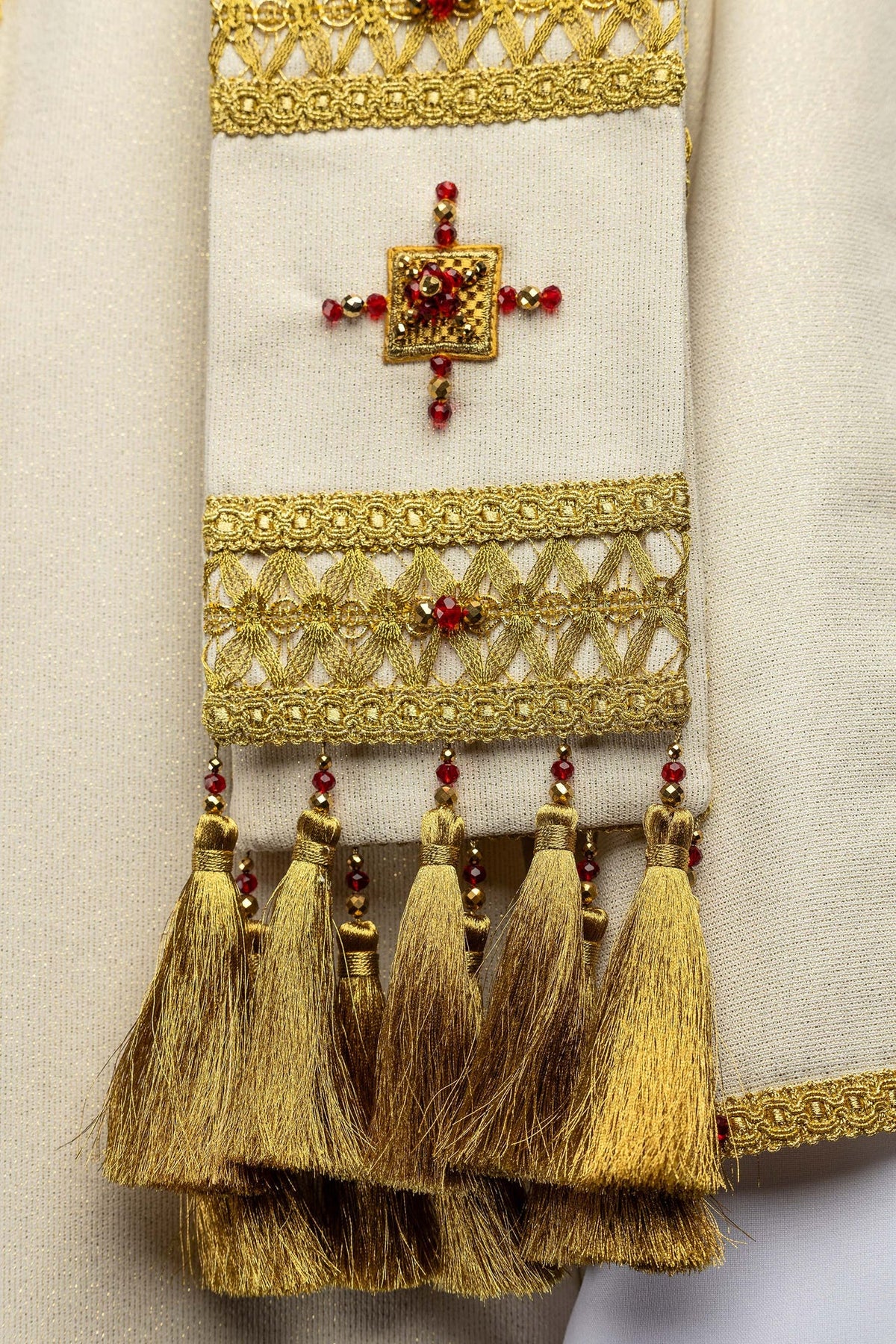Casula artesanal em close-up dos galões dourados, cruz bordada e franjas decorativas