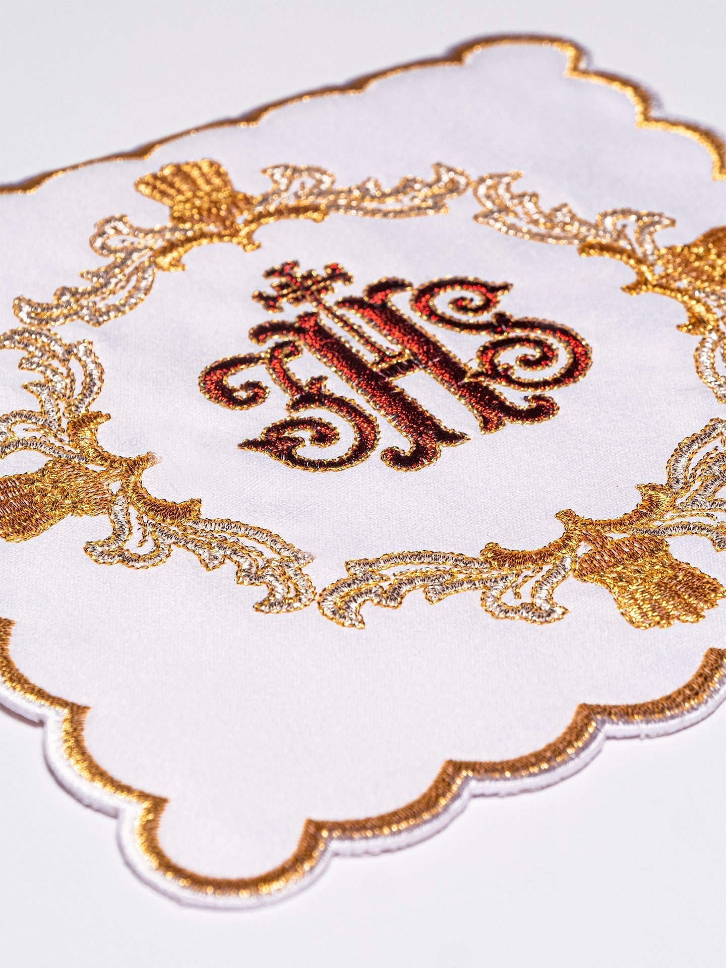 Conjunto de alfaias litúrgicas branco com bordado IHS em vermelho e dourado, incluindo pala, corporal, sanguíneo e manutérgio.