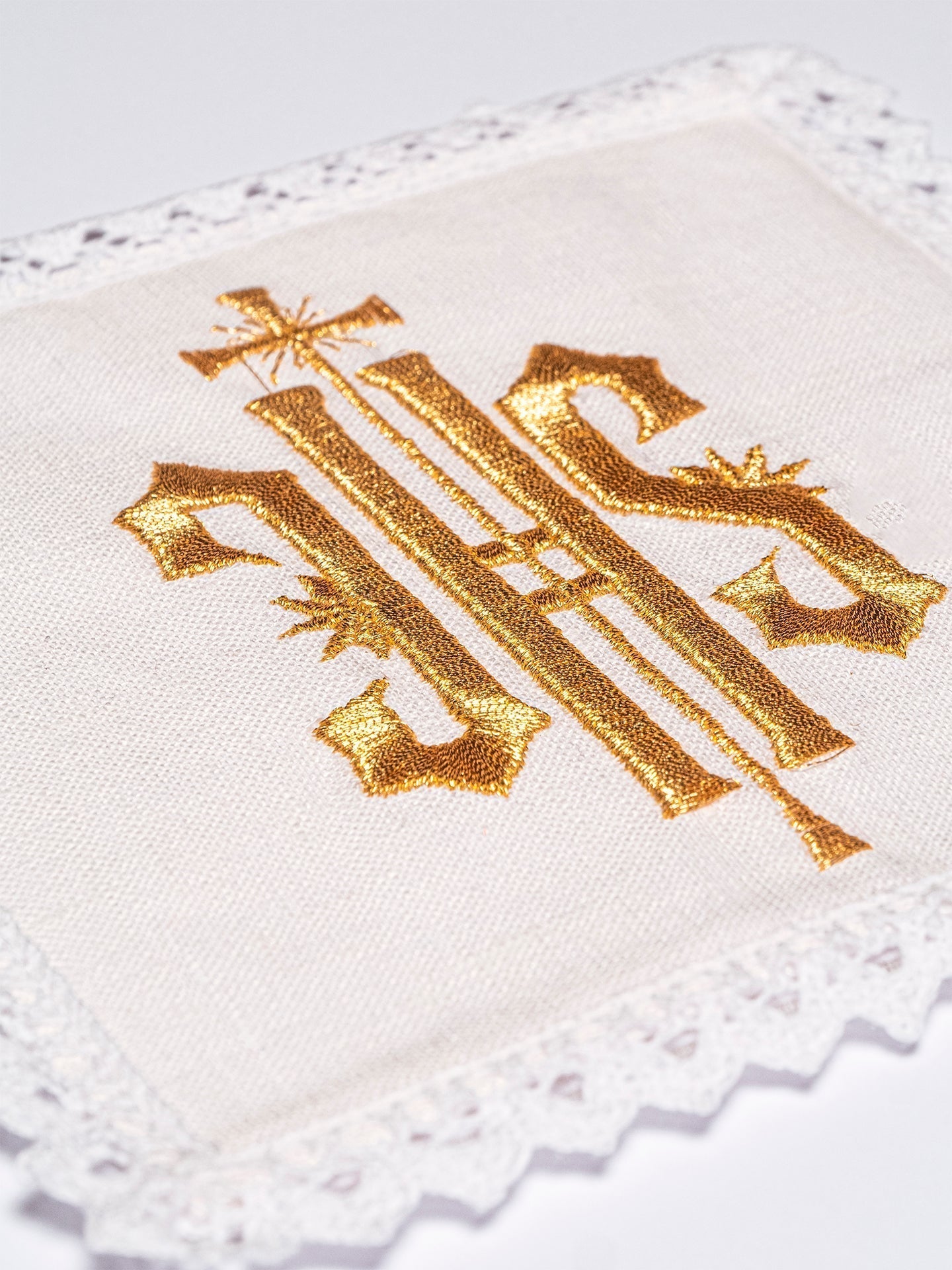Conjunto de alfaias litúrgicas em linho branco, bordado com o símbolo IHS dourado.