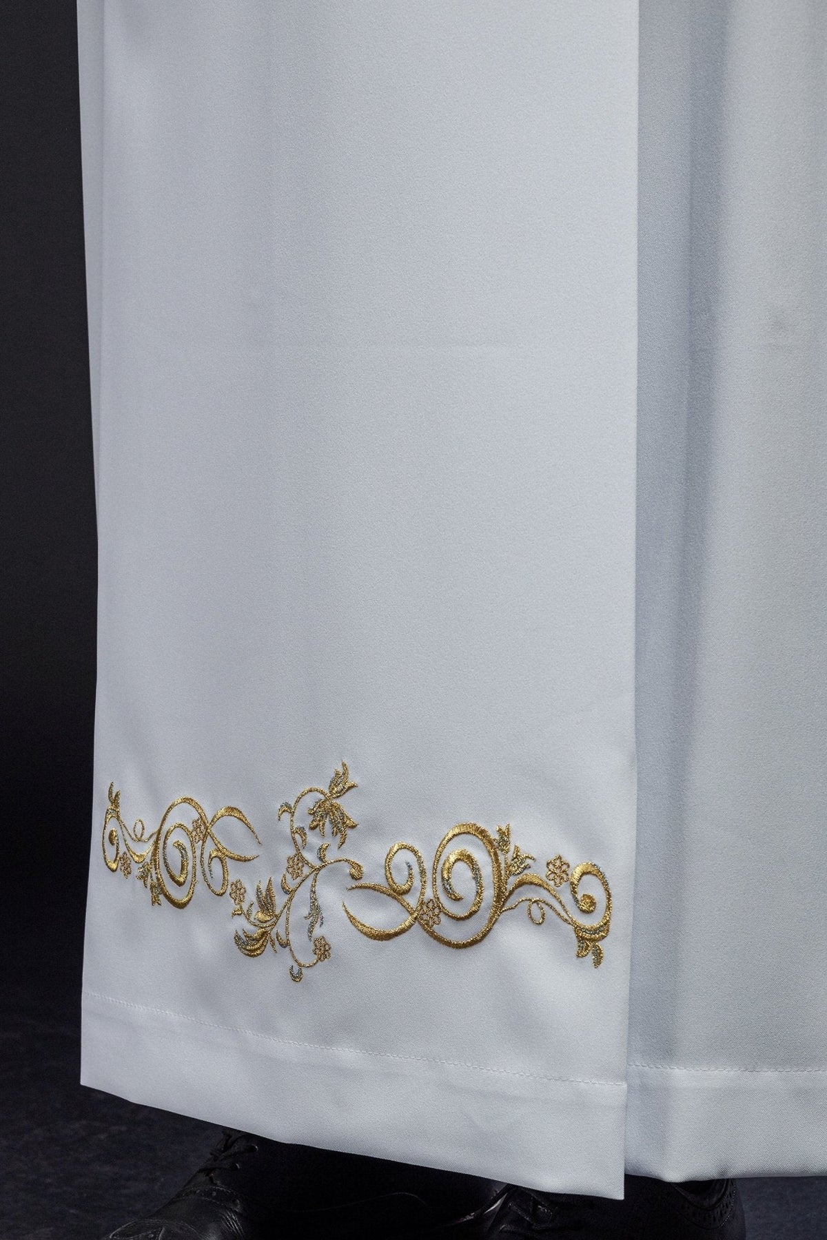Alva sacerdotal branca em close-up, com bordado dourado ornamental na barra