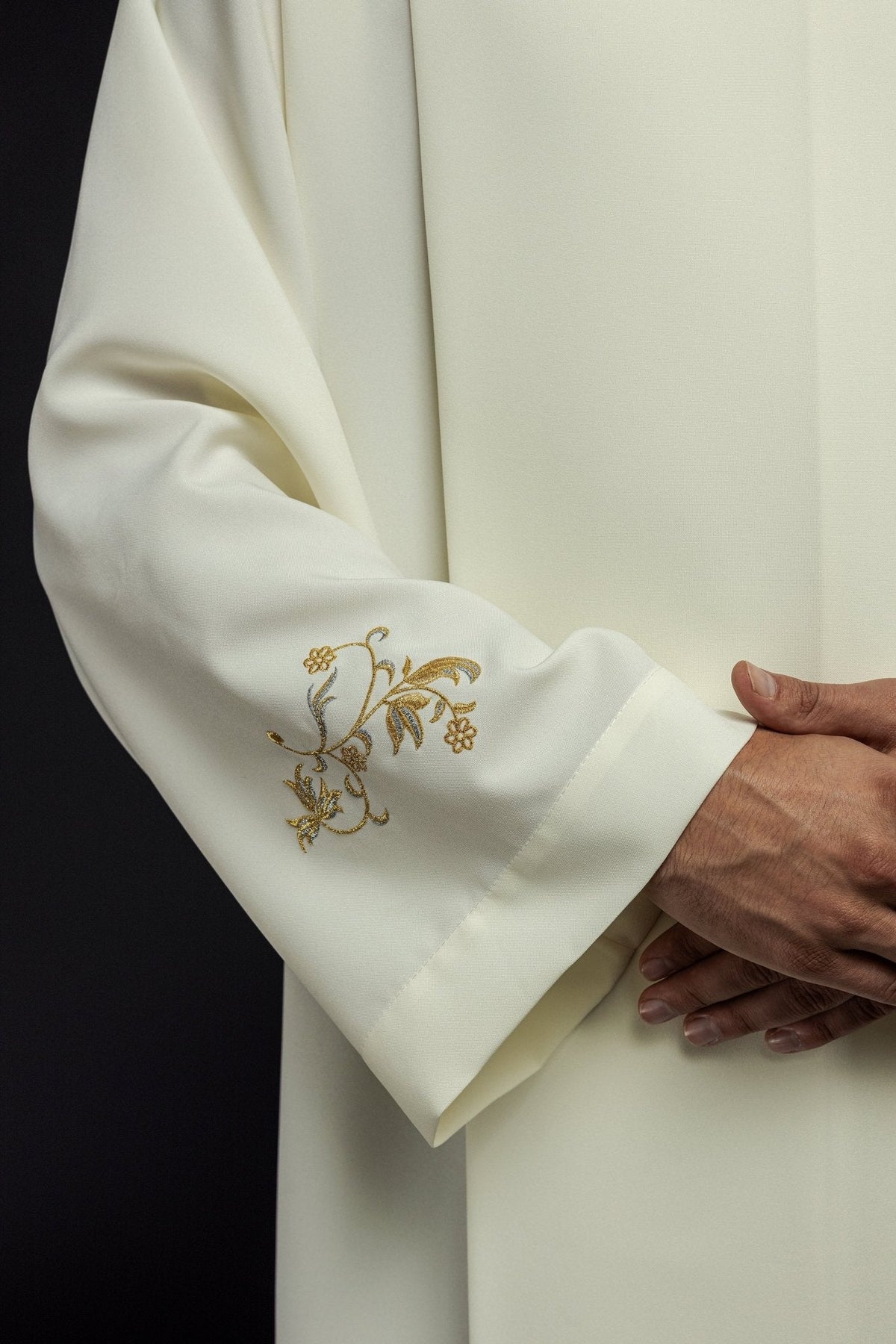 Alva sacerdotal creme em close-up, com bordado floral dourado na manga