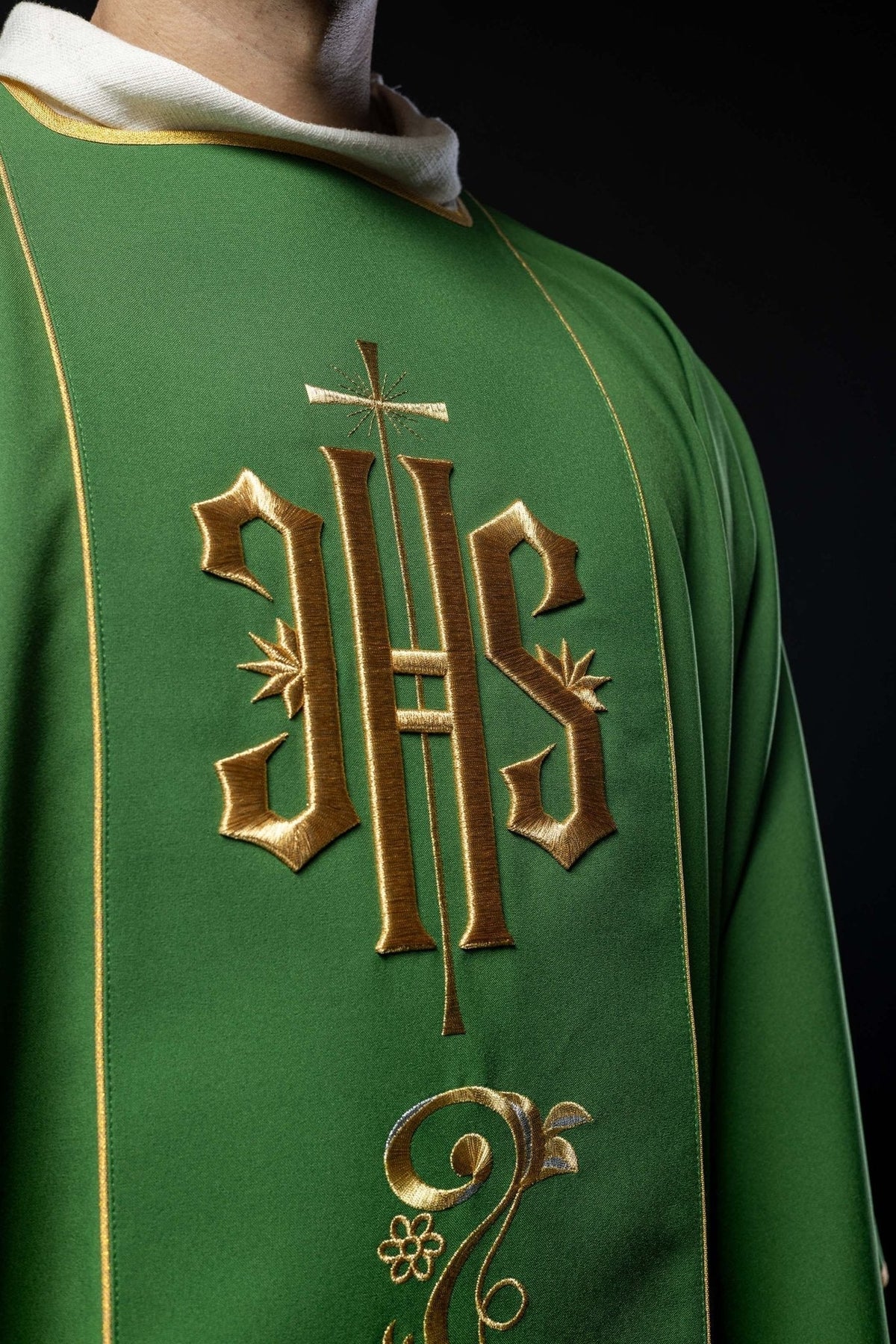 Dalmática verde em close-up frontal, com monograma IHS bordado em dourado