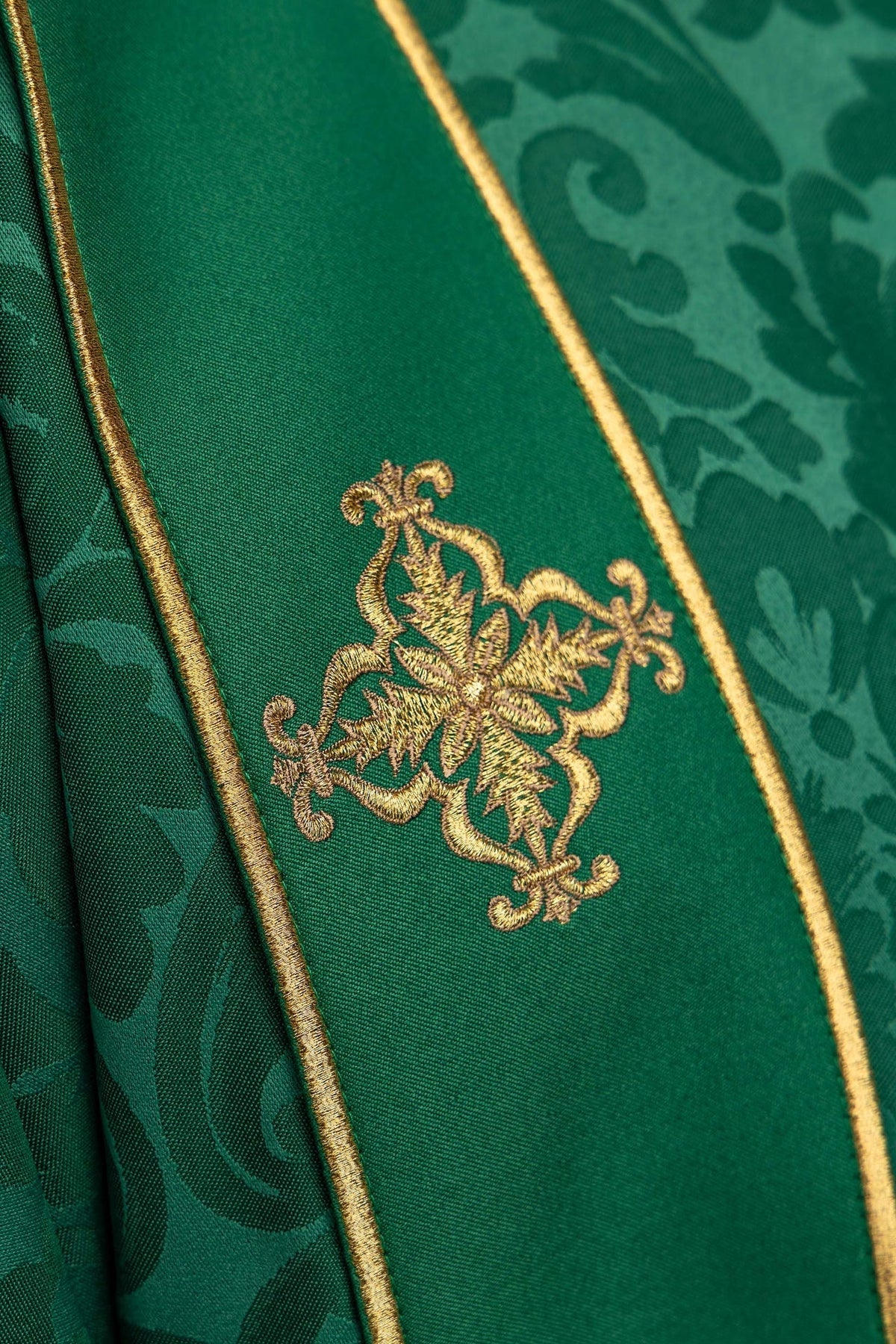 Dalmática verde com cruz bordada dourada em close-up sobre a faixa