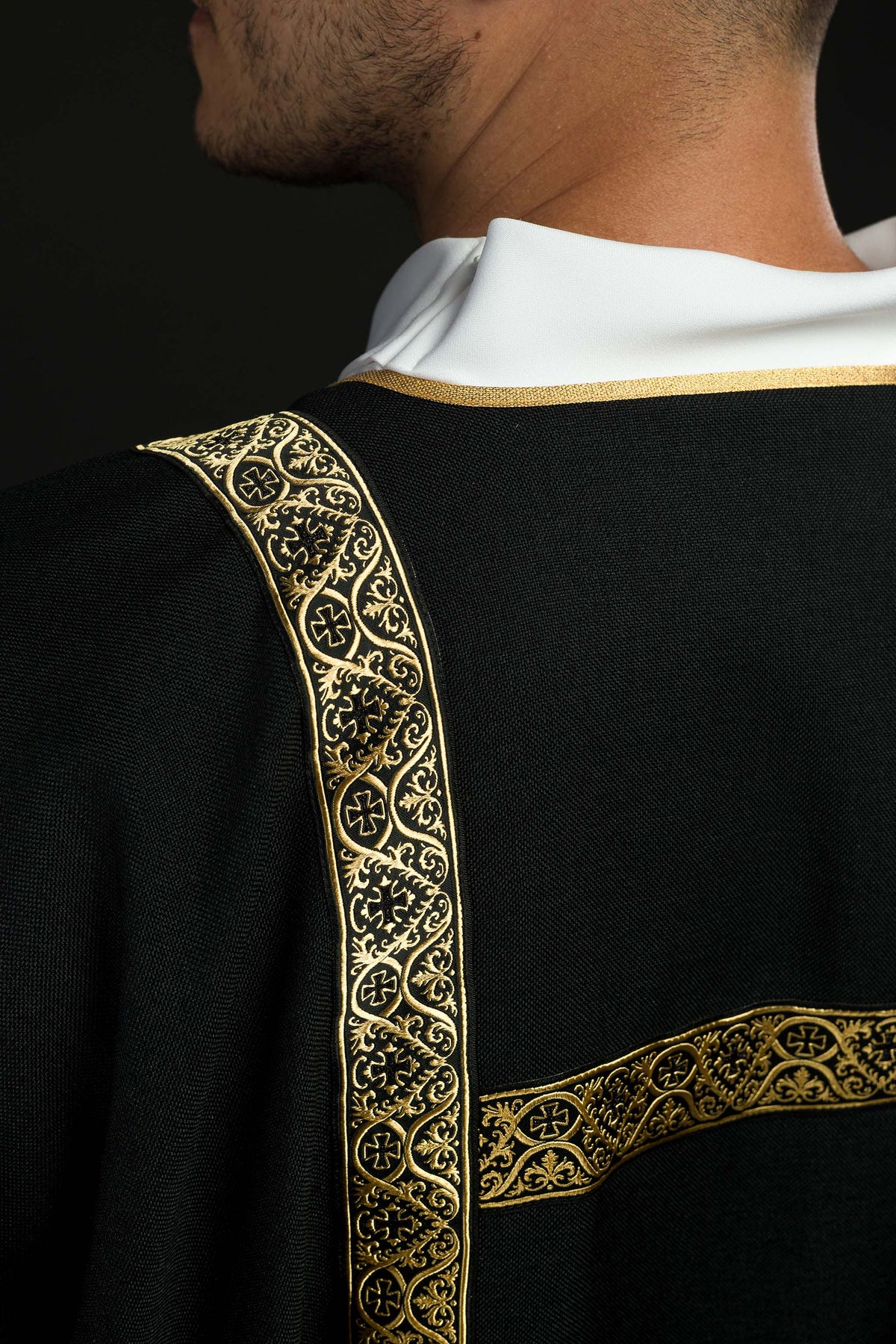 Dalmática preta com faixas de brocado dourado, detalhe do colarinho branco e faixa no ombro