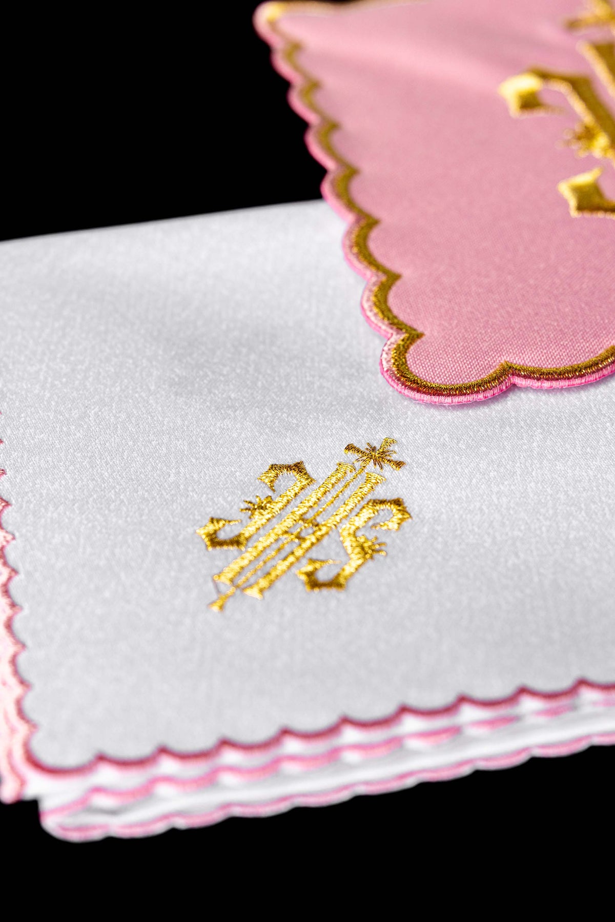 Alfaias litúrgicas brancas dobradas, com monograma IHS dourado e acabamento rosa