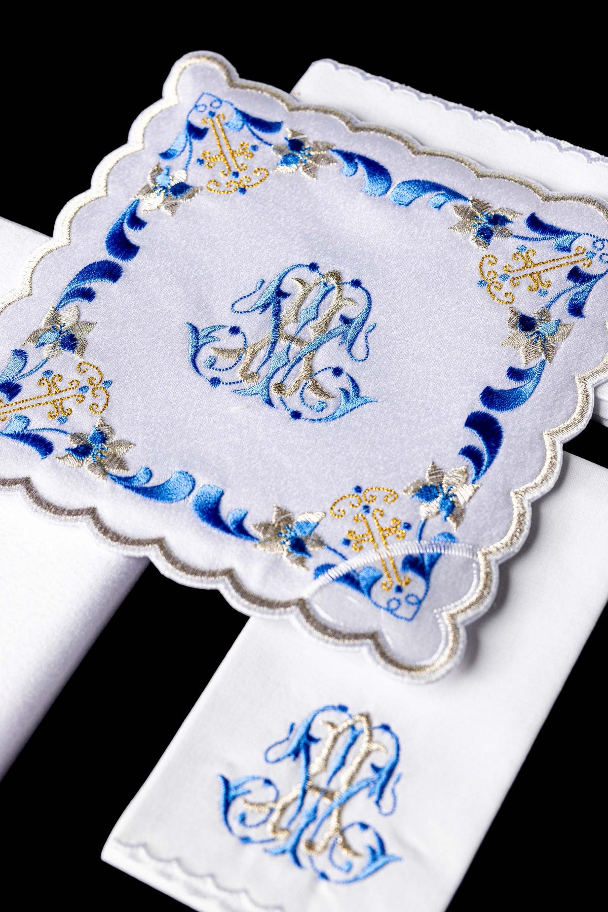 Alfaias litúrgicas brancas em close-up, com bordado mariano azul e dourado