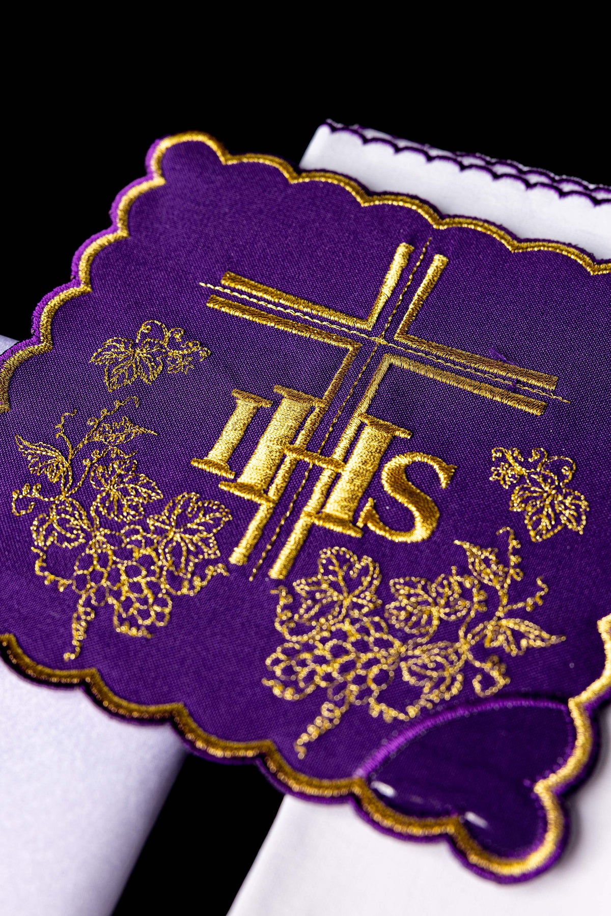 Conjunto de alfaias litúrgicas com detalhe aproximado do bordado roxo IHS, cruz e cachos de uva dourados