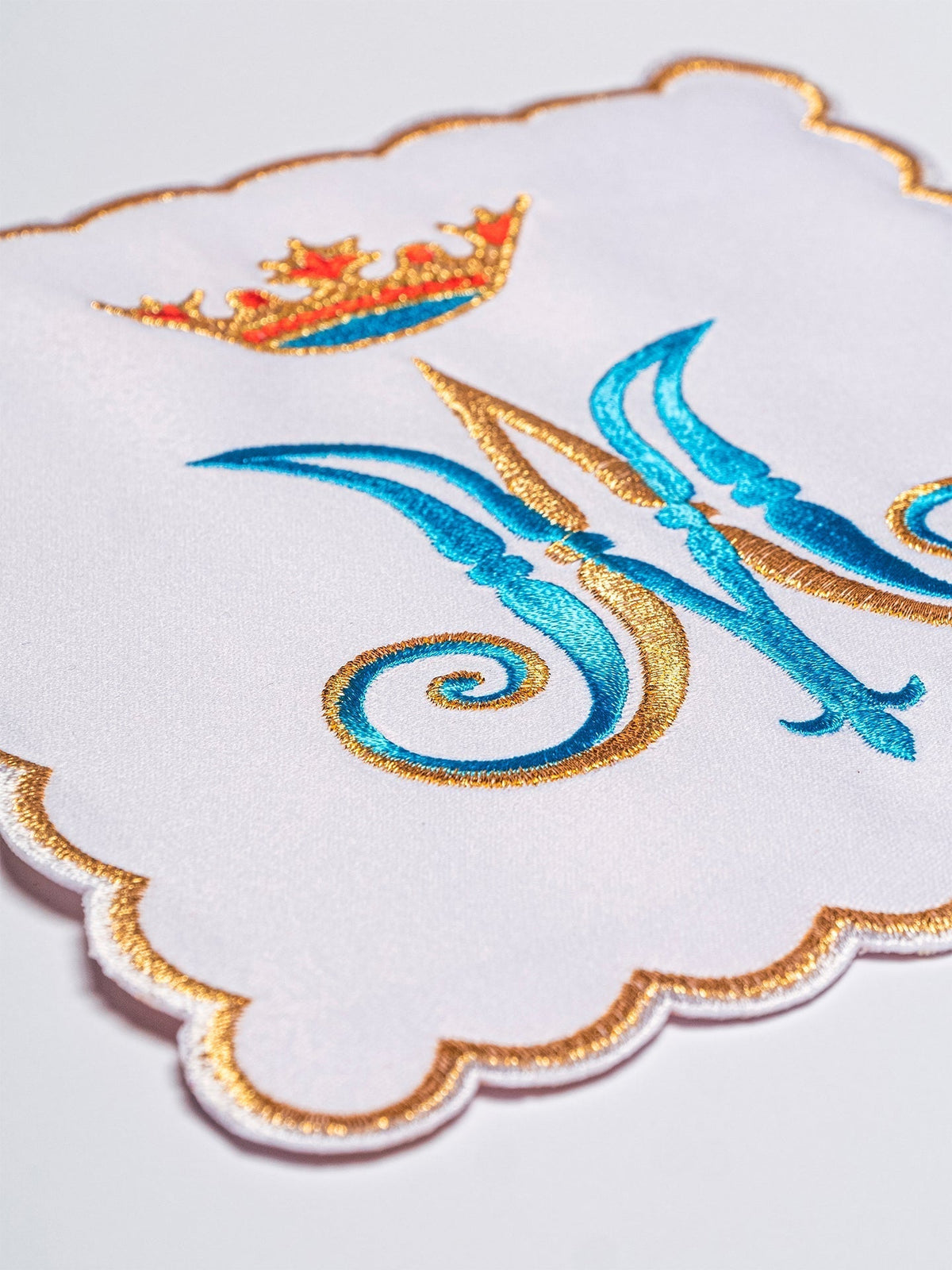 Alfaias litúrgicas bordadas com detalhe aproximado do monograma mariano azul e dourado