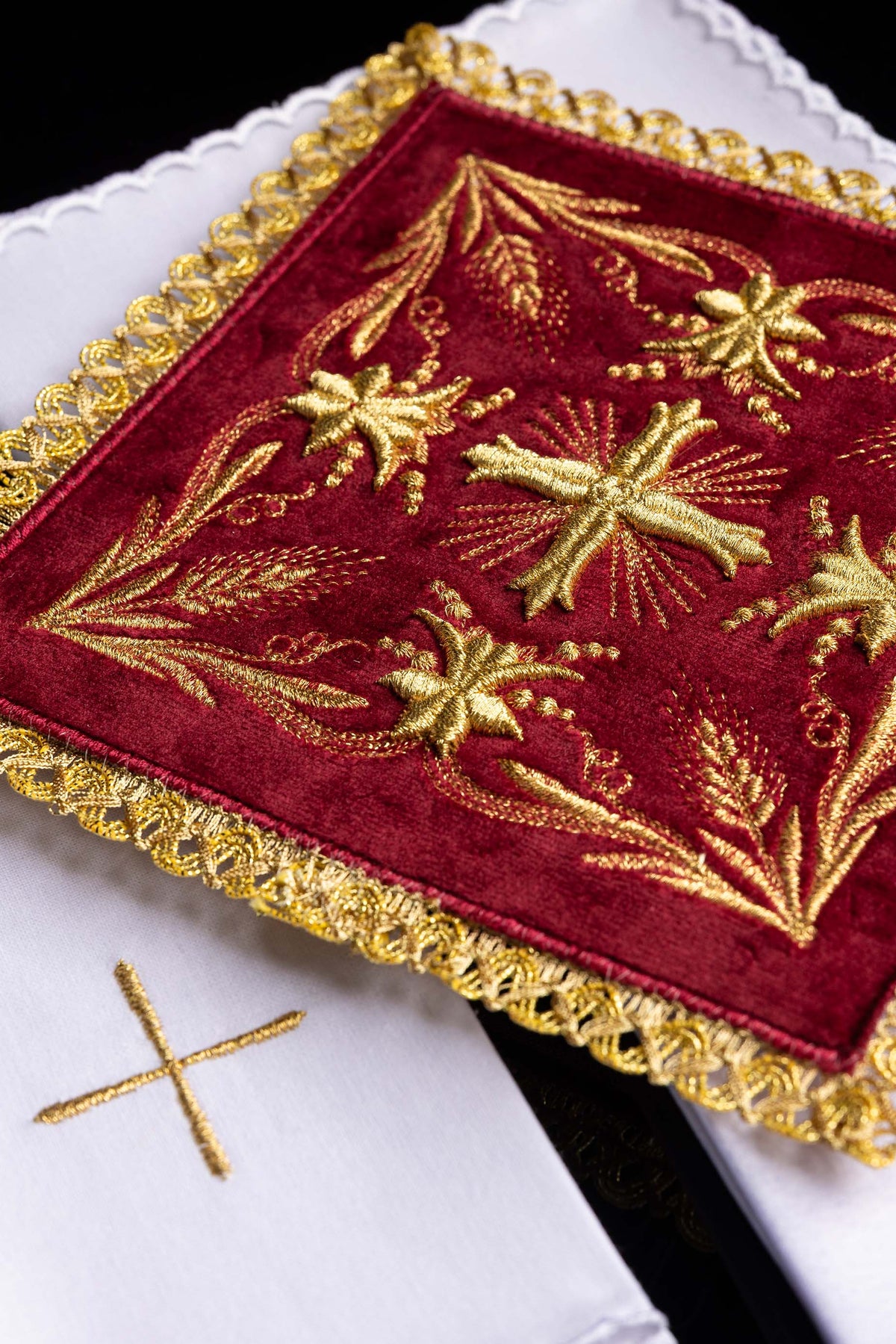 Pala de veludo vermelha com bordado dourado sobre alfaias litúrgicas brancas