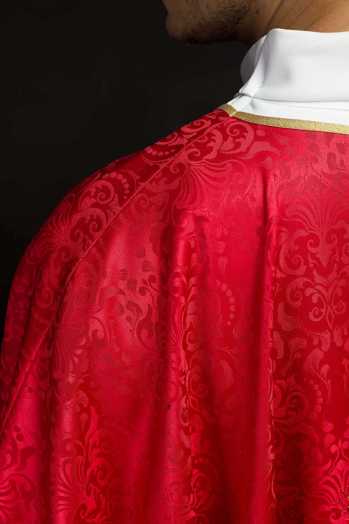 Casula vermelha jacquard em close-up, mostrando o padrão ornamental do tecido e gola dourada