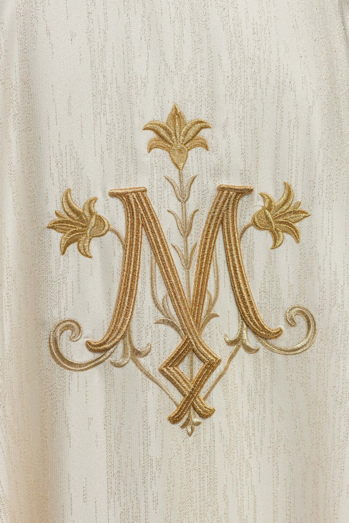 Casula creme mariana em close-up, com monograma e flores douradas bordados
