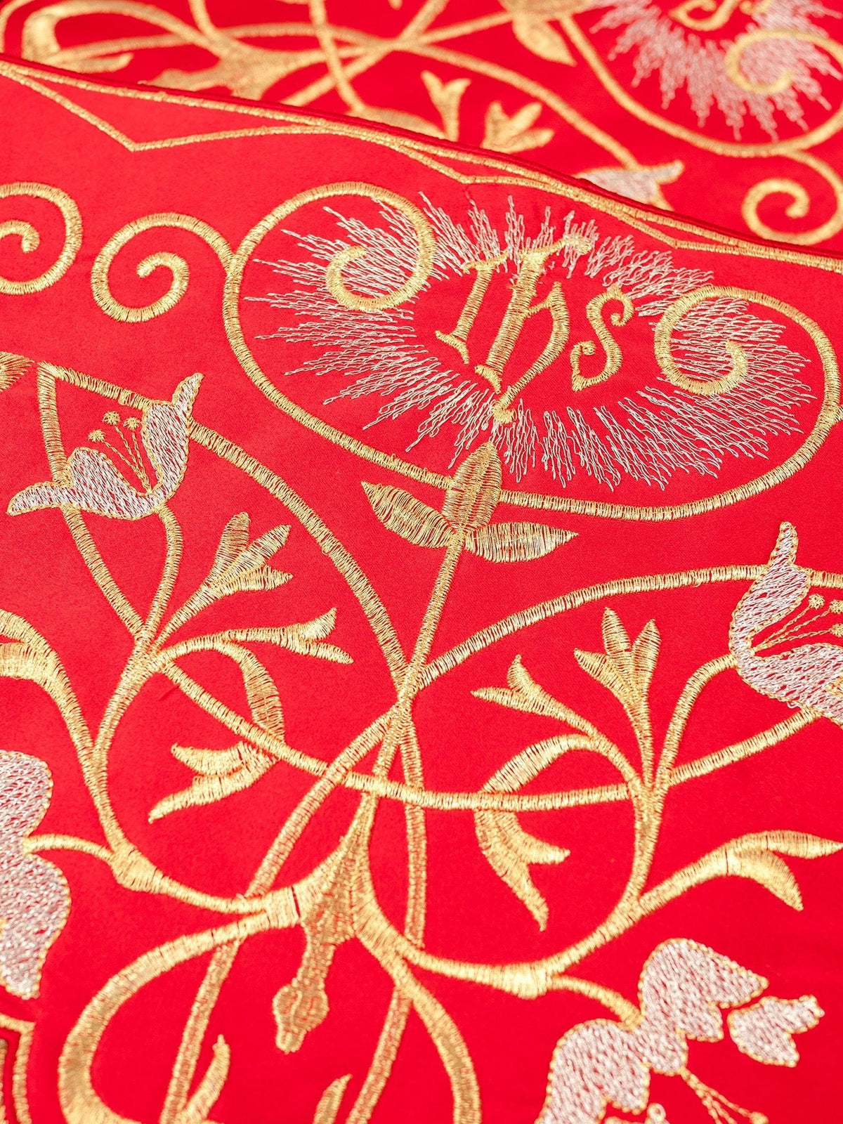 Renda vermelha para toalha de altar em close-up, com monograma IHS e motivos florais bordados
