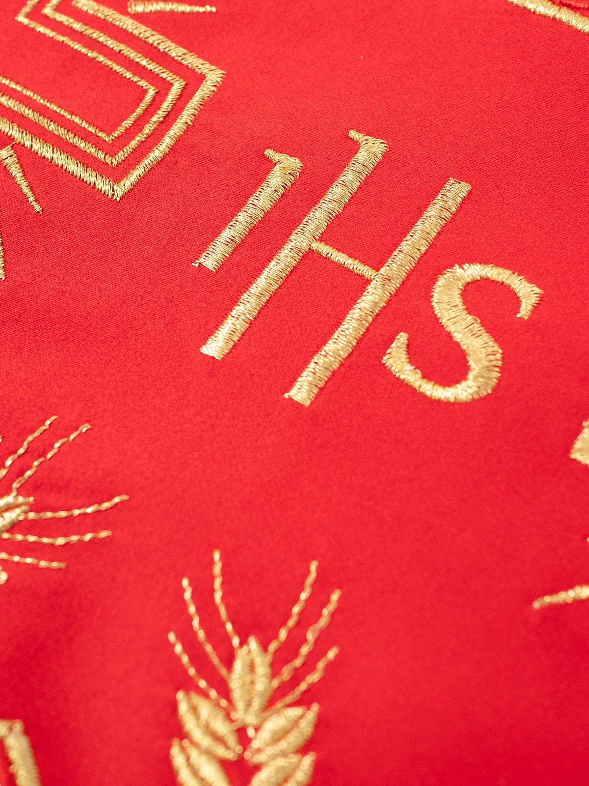 Tecido com monograma IHS, close-up do bordado dourado sobre fundo vermelho