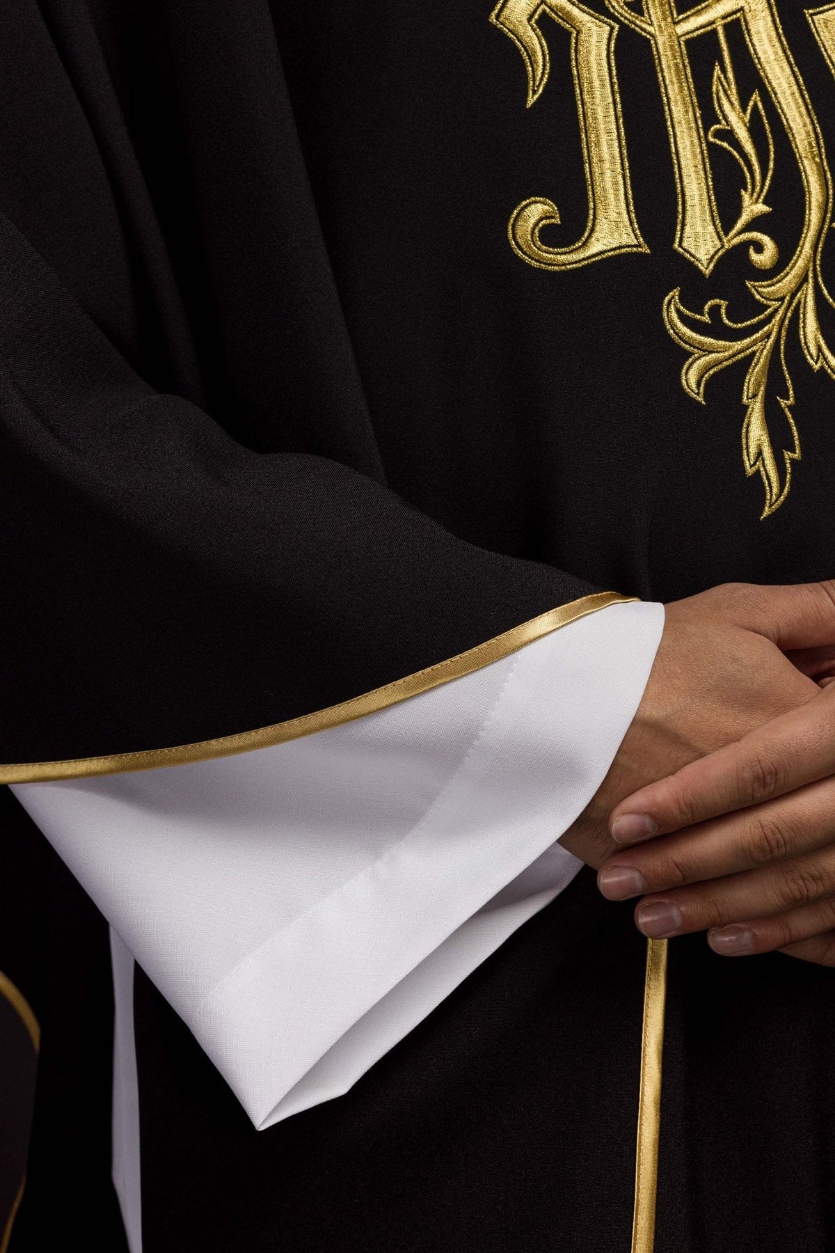Casula preta bordada IHS em detalhe da manga, com forro branco e acabamento dourado