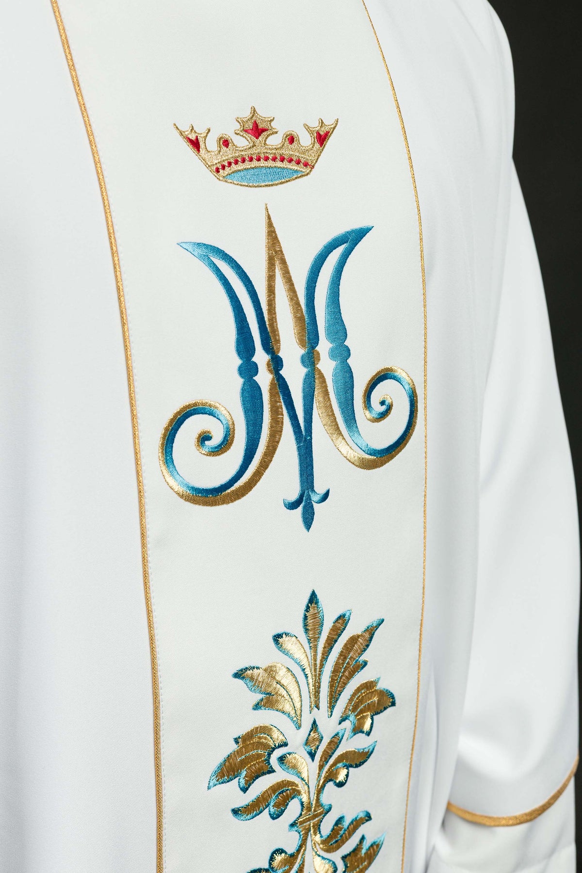 Casula branca com bordado mariano em close, destacando a coroa e o monograma azul e dourado