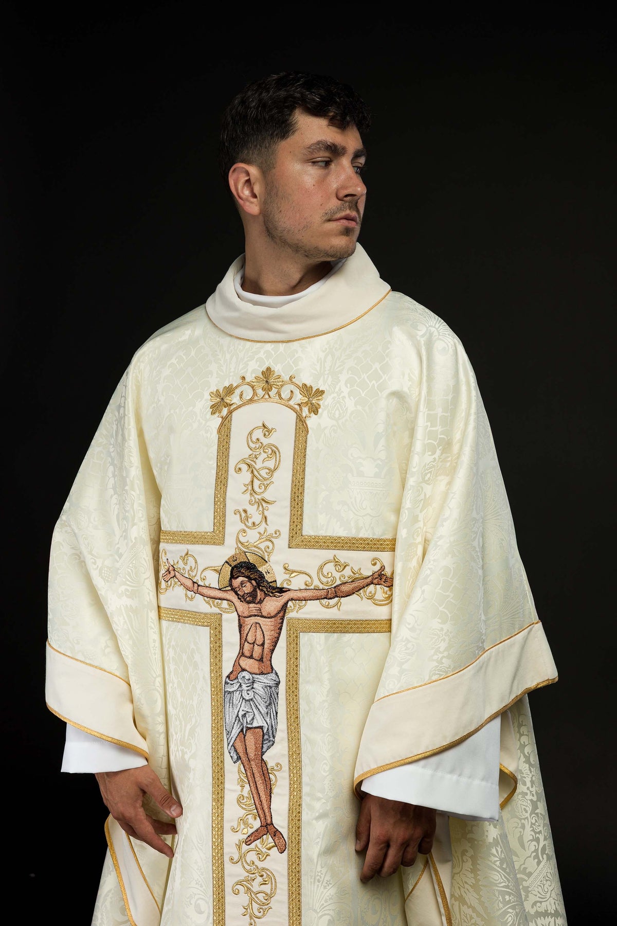 Casula creme vista frontal aproximada, com cruz dourada e imagem bordada de Jesus Cristo crucificado