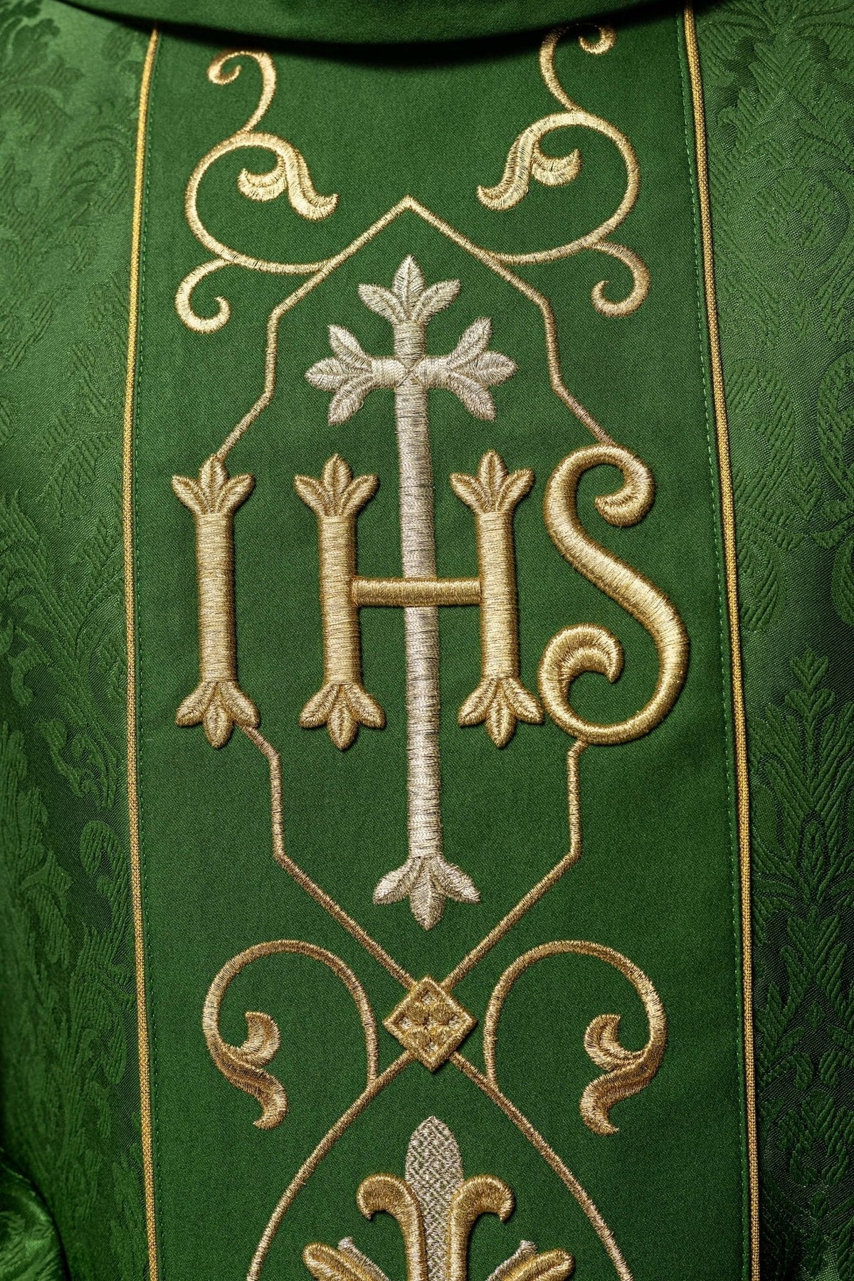Casula verde com IHS bordado em close-up, mostrando o monograma IHS e a cruz
