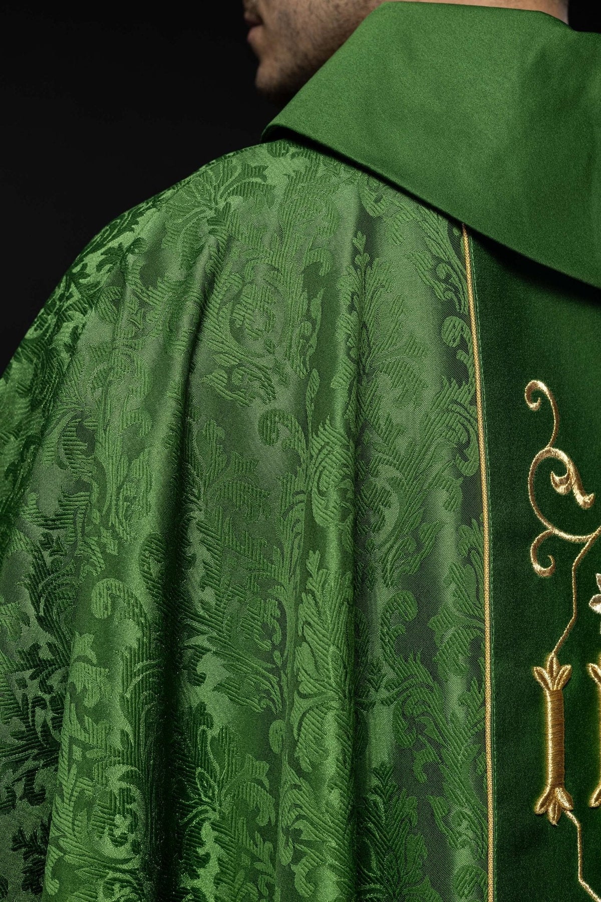 Casula verde com IHS bordado em detalhe lateral, mostrando o tecido adamascado verde