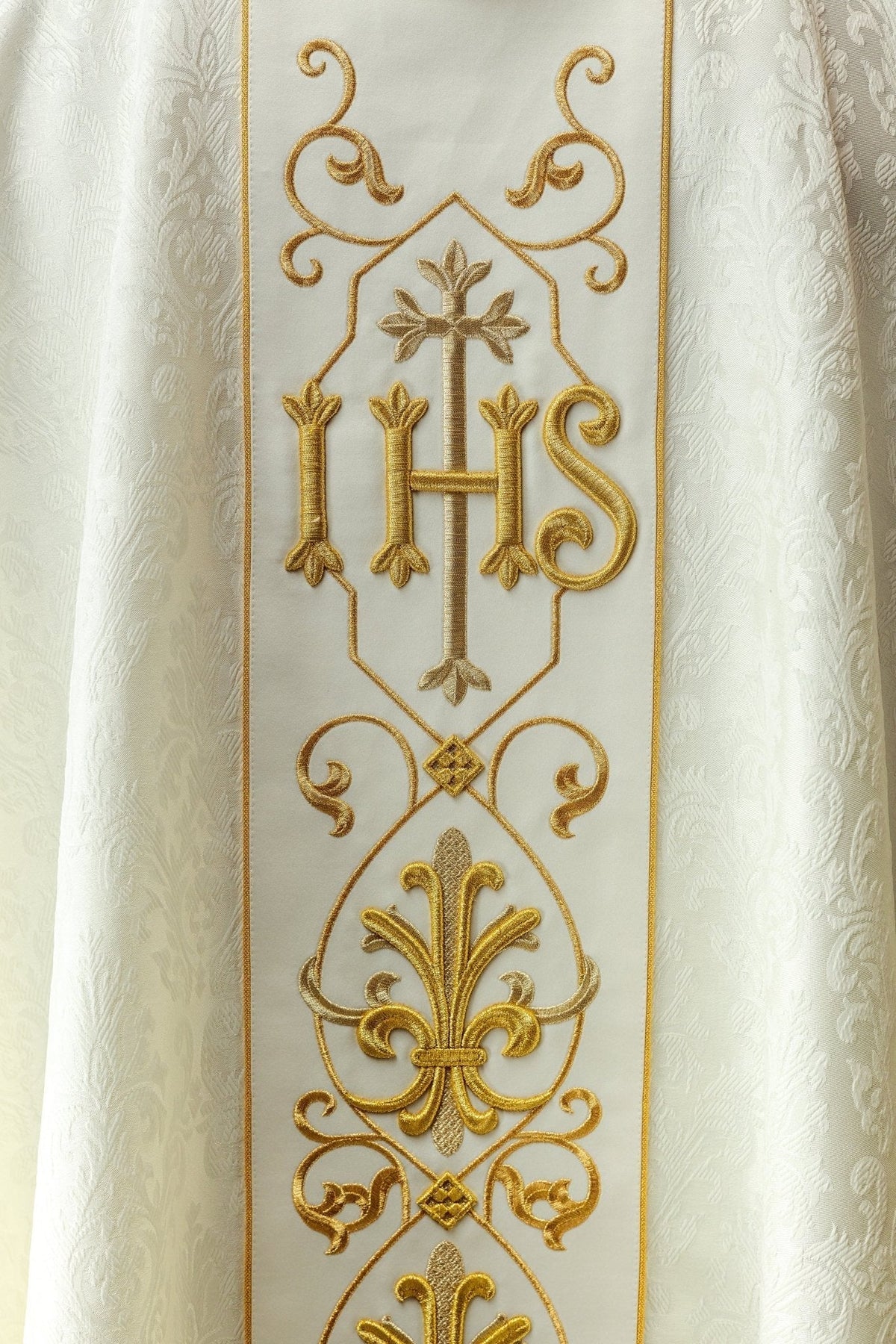 Casula creme com símbolo IHS bordado, close-up da faixa frontal e ornamentos dourados