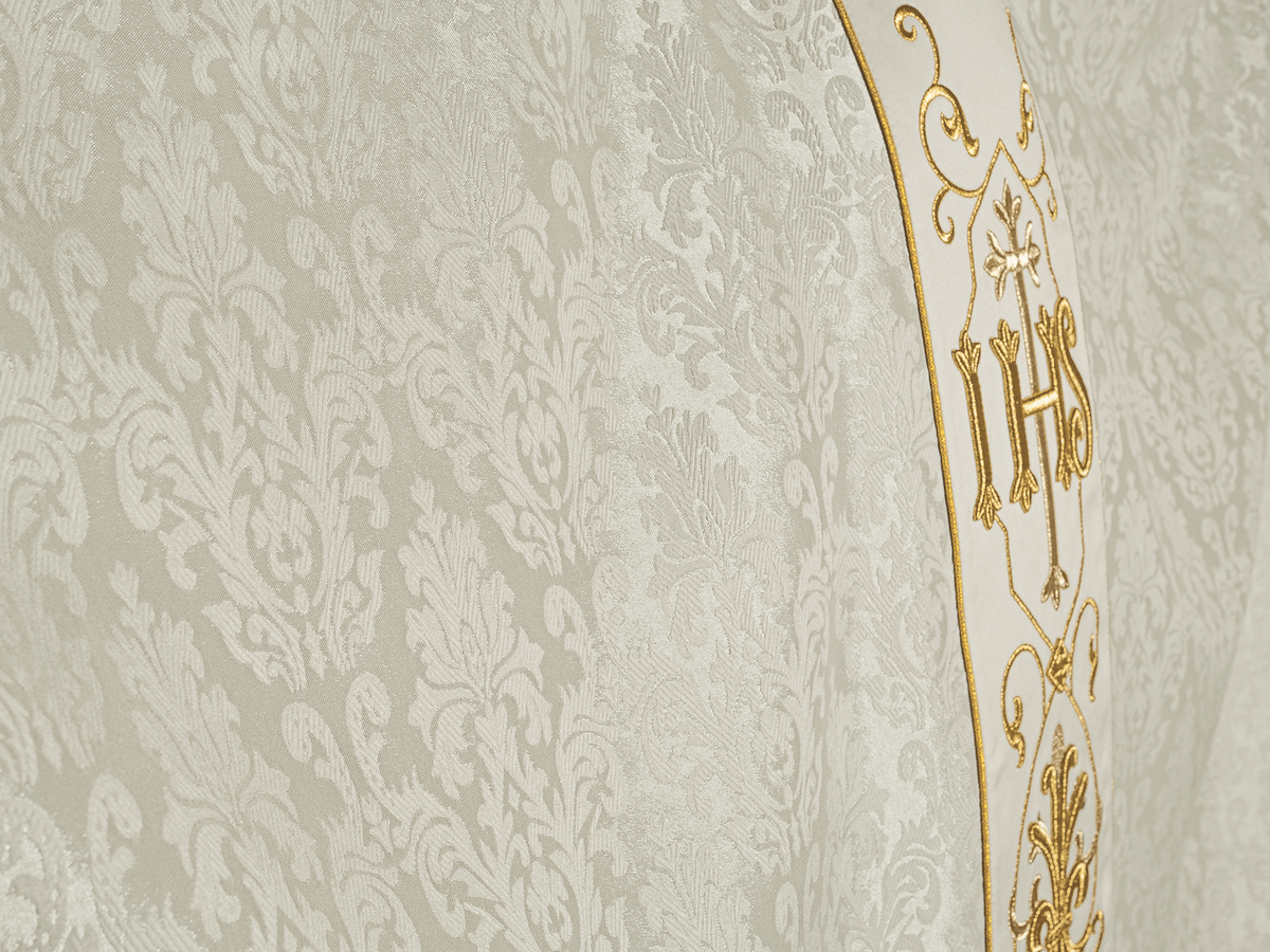 Casula creme com símbolo IHS, close-up do tecido decorativo e bordado dourado