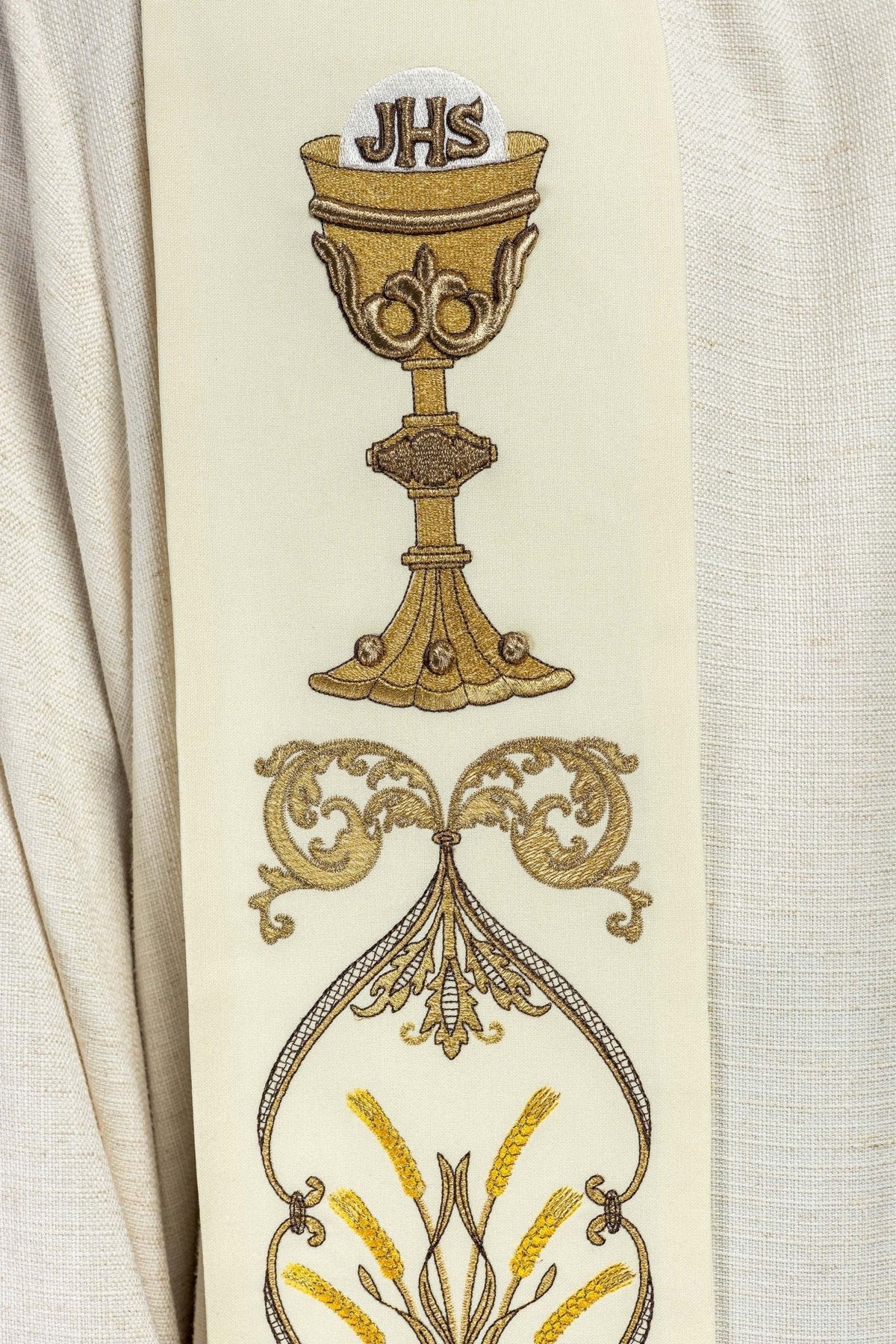 Estola sacerdotal creme em close-up, destacando cálice IHS e espigas bordadas
