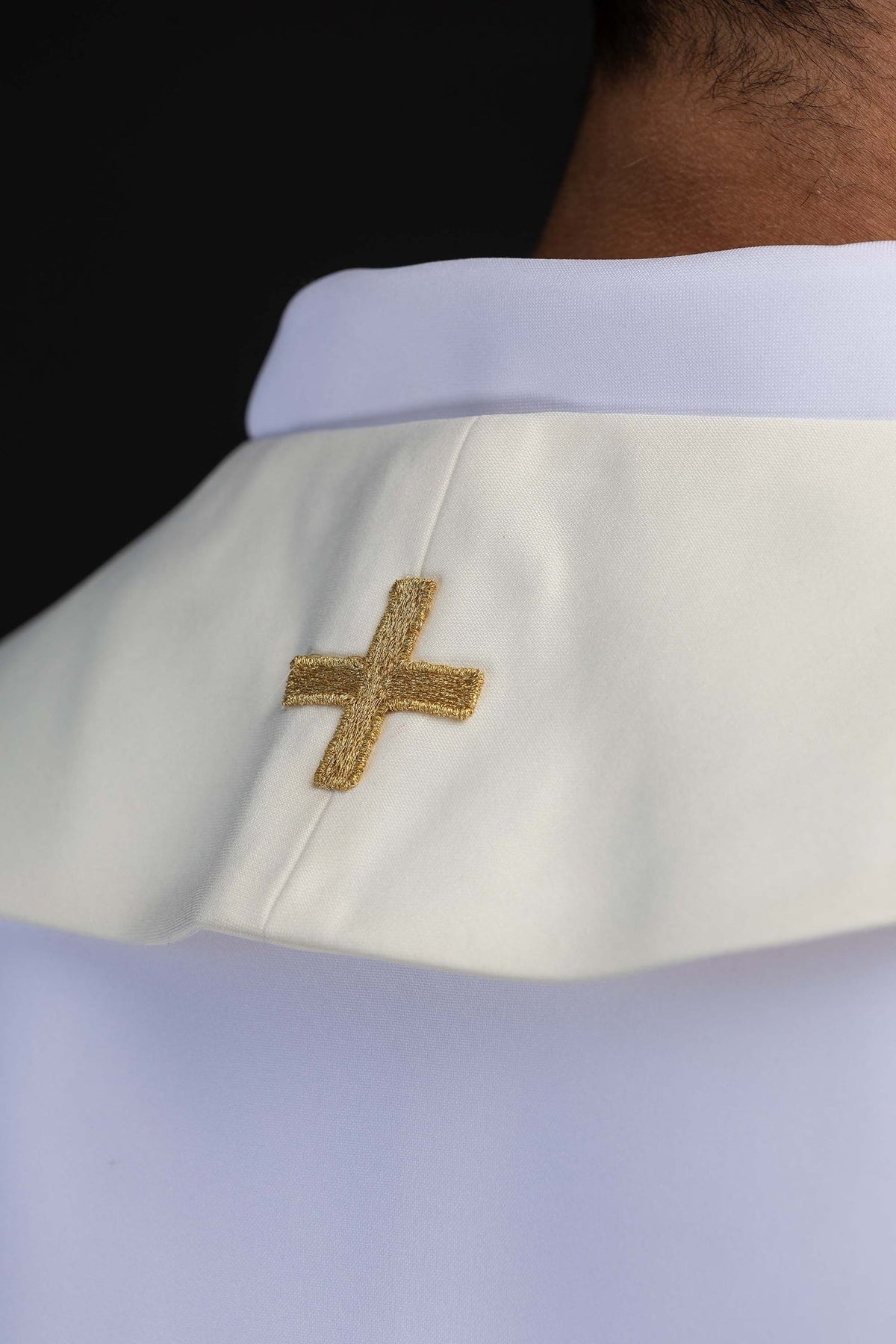 Estola marfim ecru, detalhe da cruz dourada bordada próxima ao colarinho