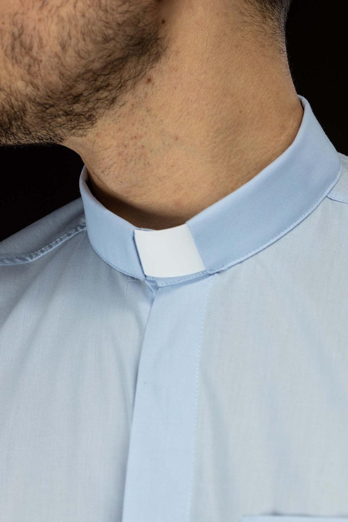 Camisa clerical azul em close-up do colarinho romano com detalhe branco