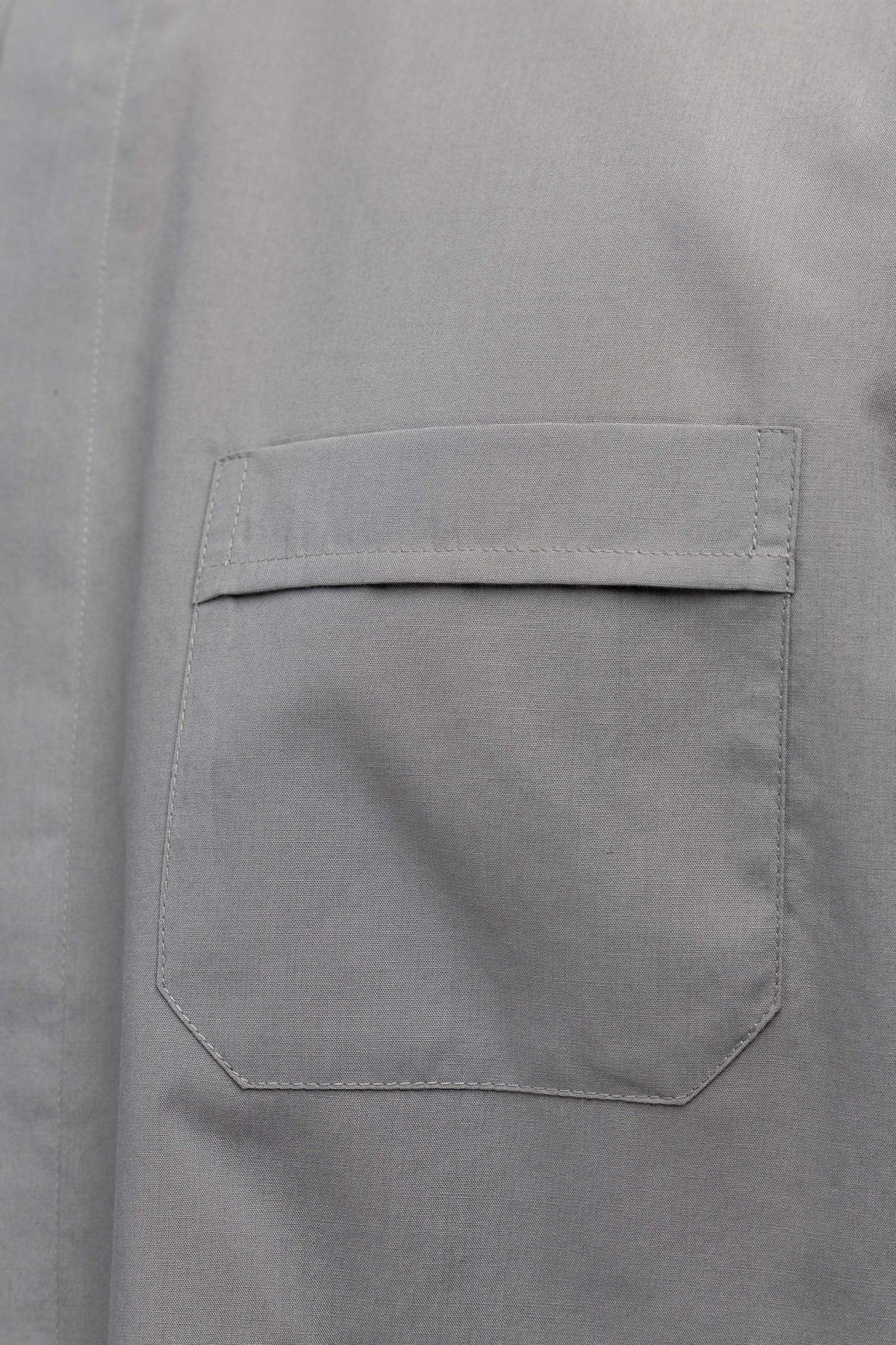 Camisa clerical cinza-clara com close-up do bolso frontal com aba