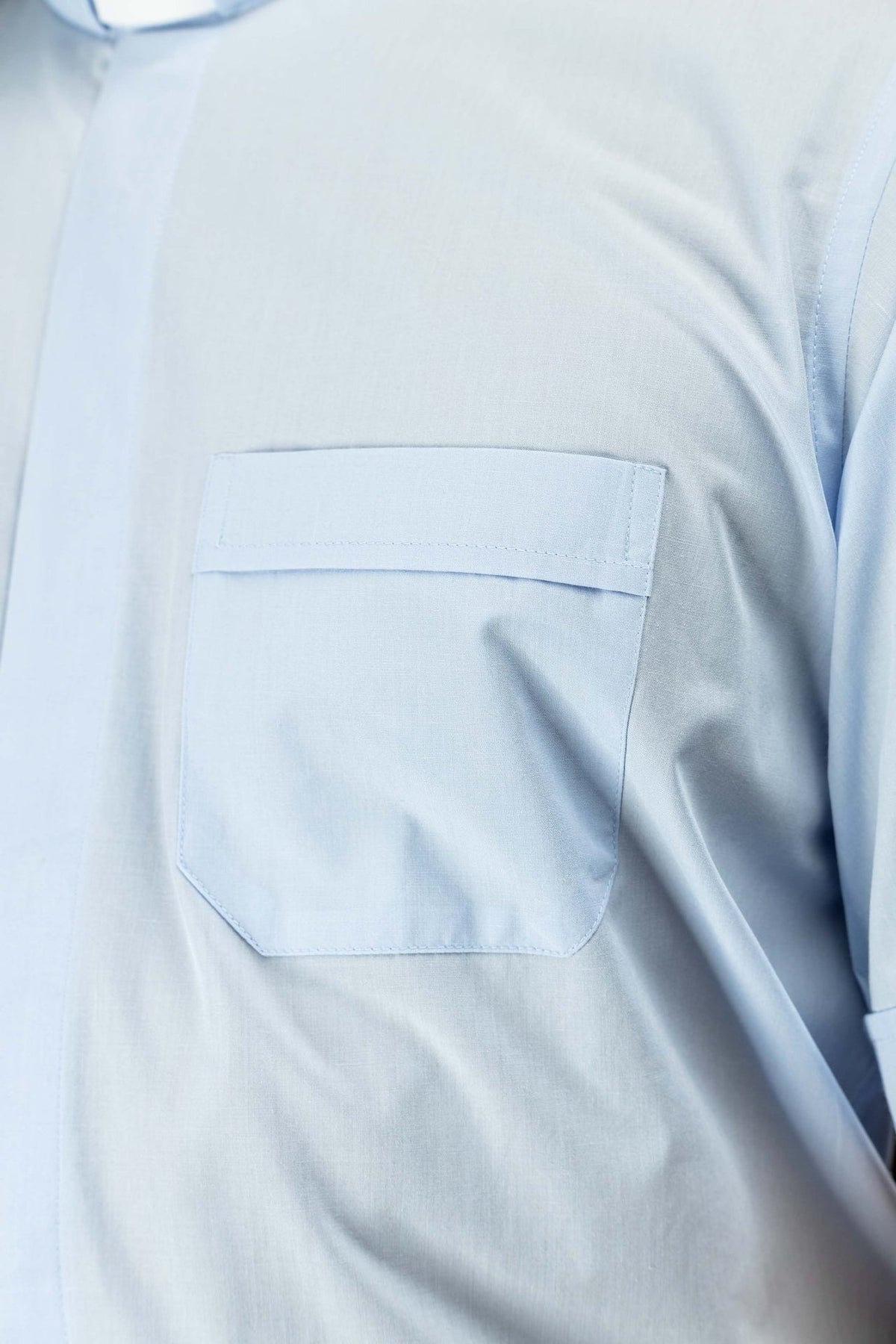 Camisa clerical azul-clara em close-up do bolso frontal com aba e cantos inferiores chanfrados