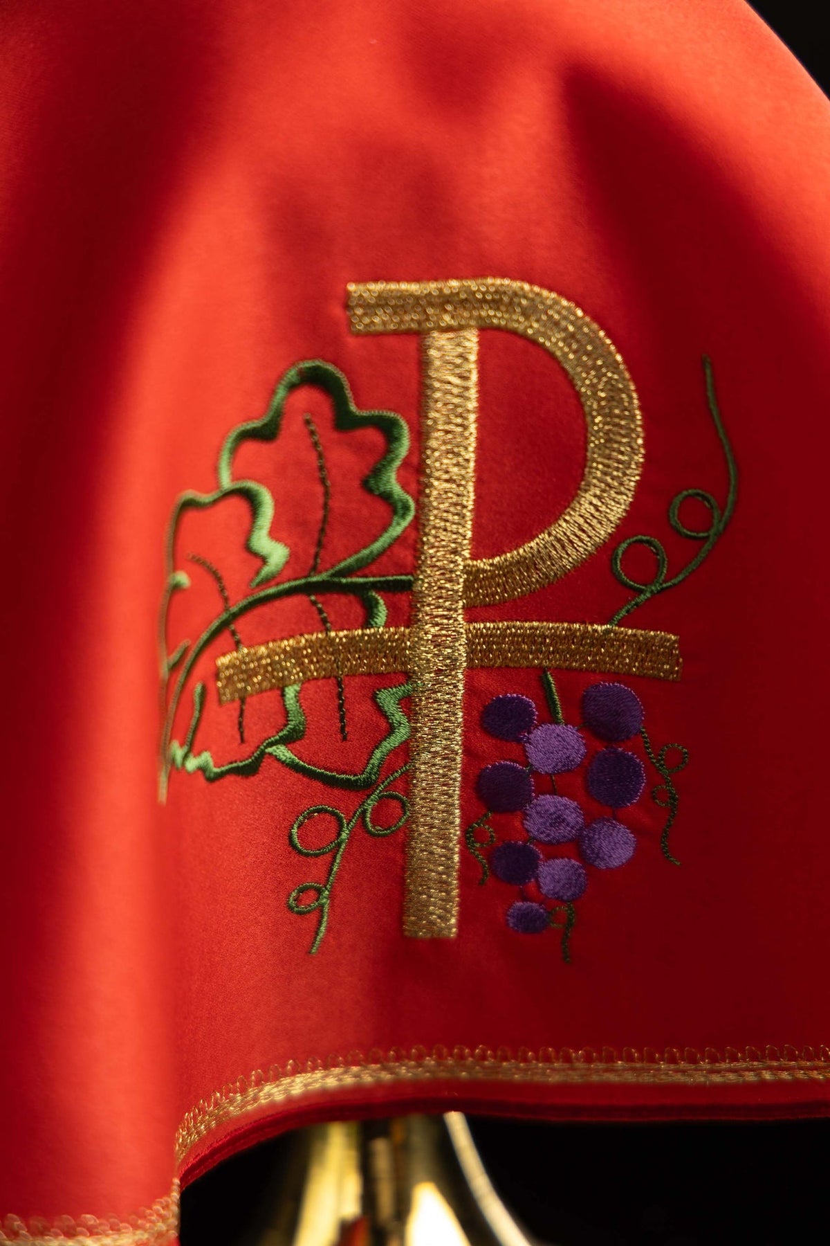 Véu de âmbula vermelho em close-up, bordado PAX dourado com videira e uvas