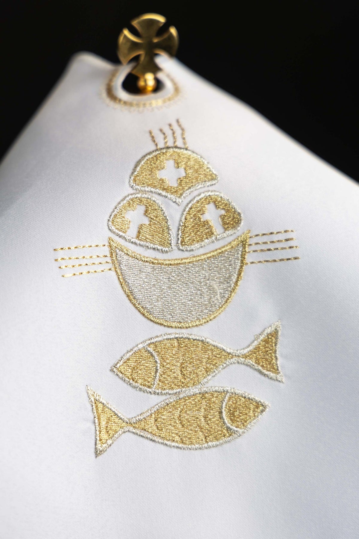 Véu de âmbula com close do bordado dourado de pão, hóstia e peixes