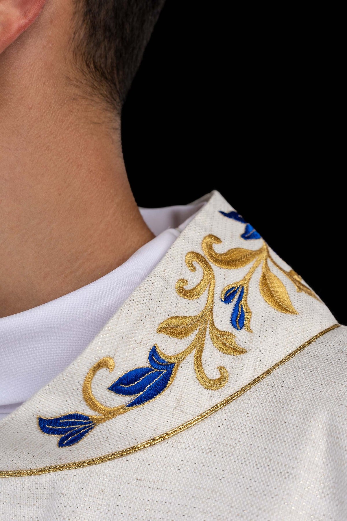 Dalmática marfim ecru em close-up do colarinho com bordado floral azul e dourado