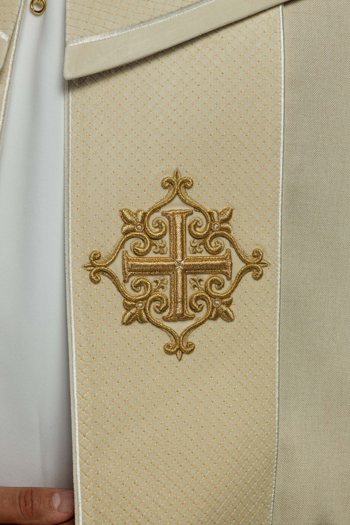 Faixa creme da capa de asperges com bordado de cruz dourada em close