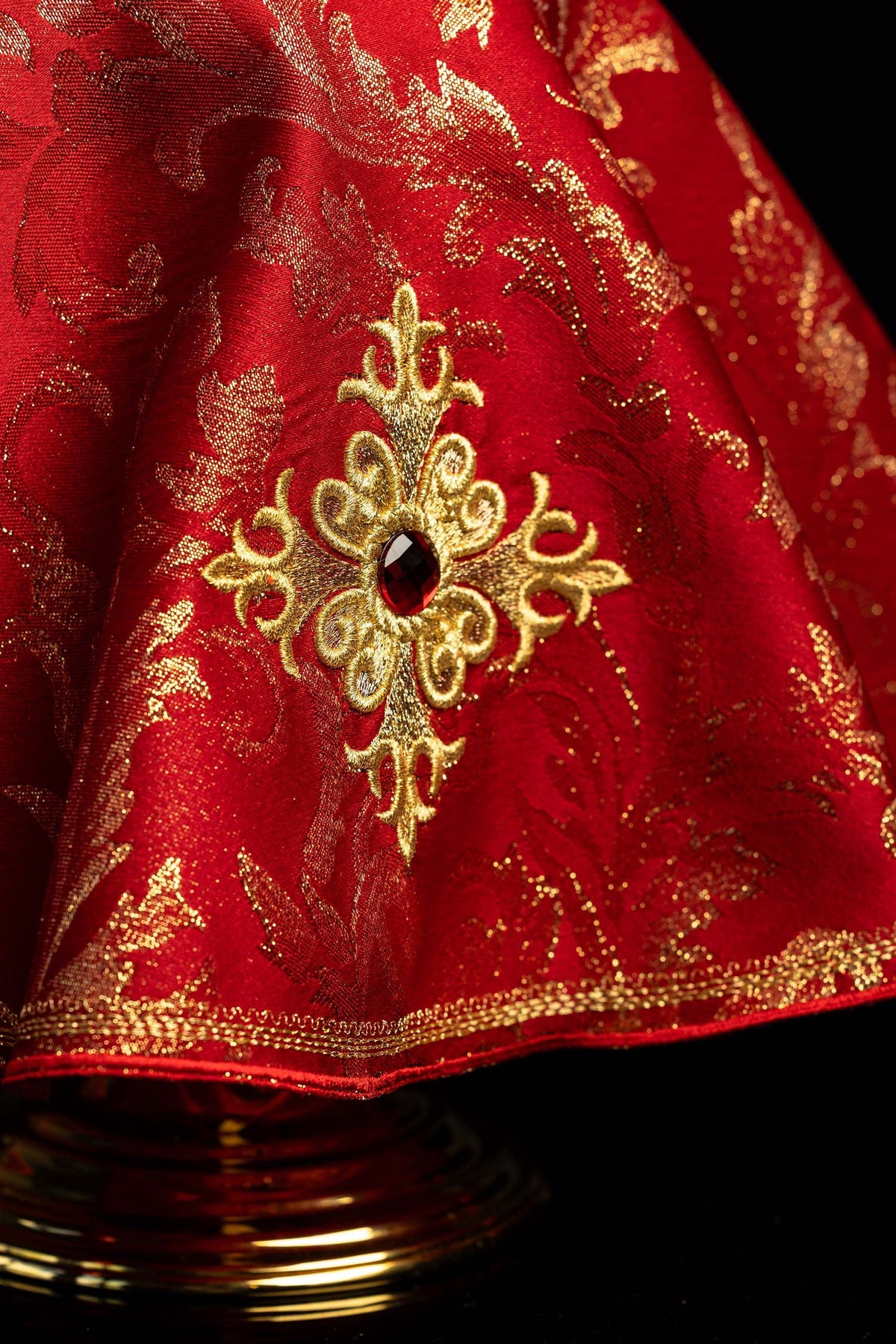 Véu de âmbula vermelho em close-up, com cruz bordada e pedra decorativa
