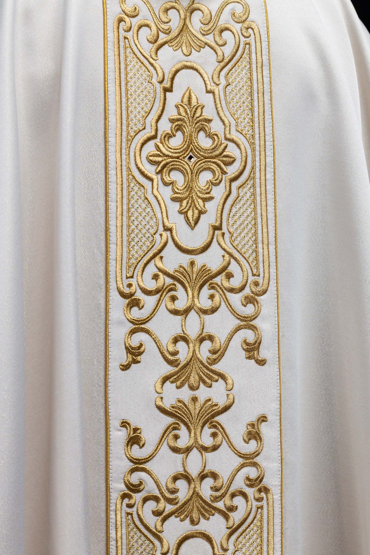 Casula branca em close-up, destacando o bordado dourado ornamental da faixa