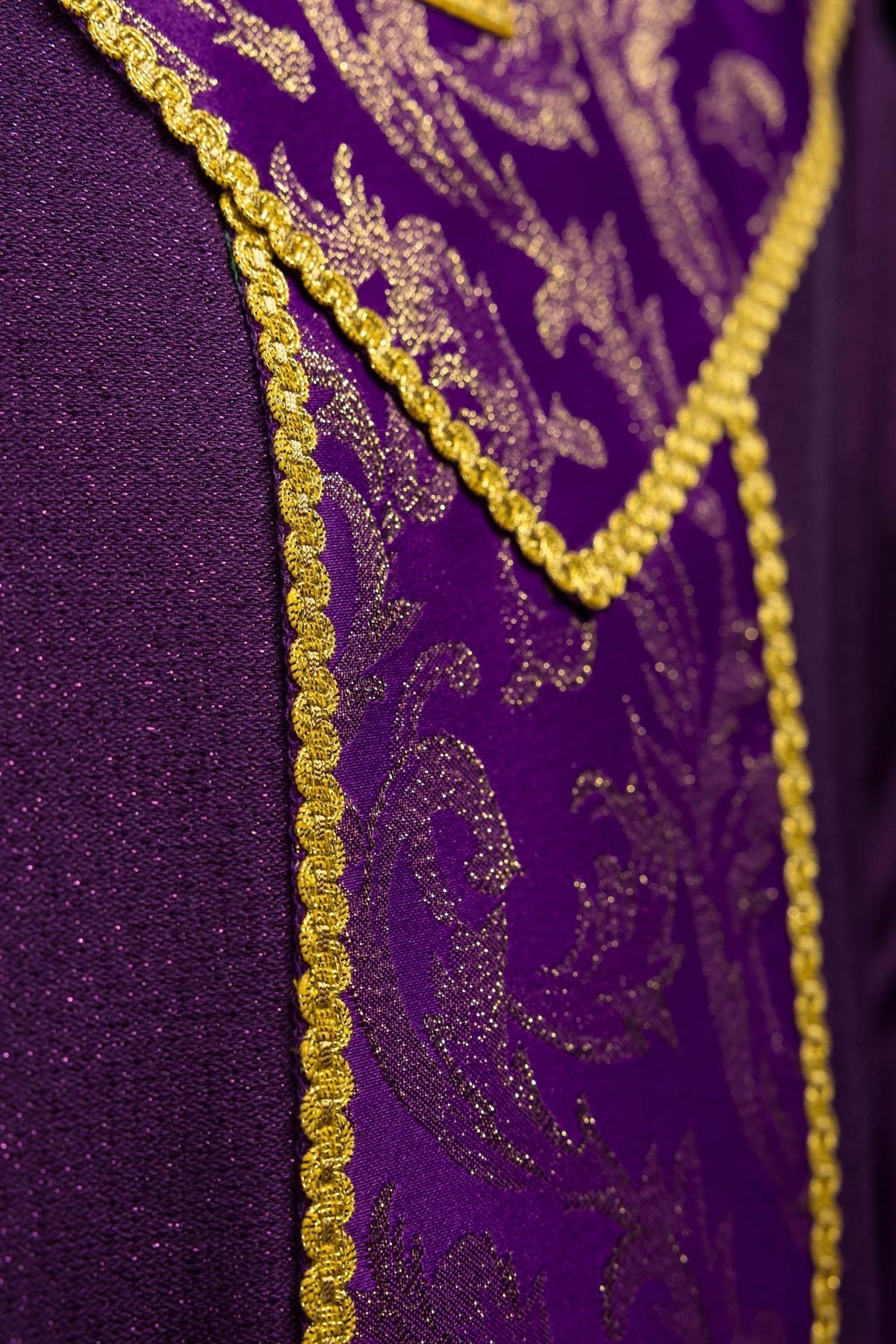 Casula roxa em close-up lateral, destacando tecido jacquard e galão dourado