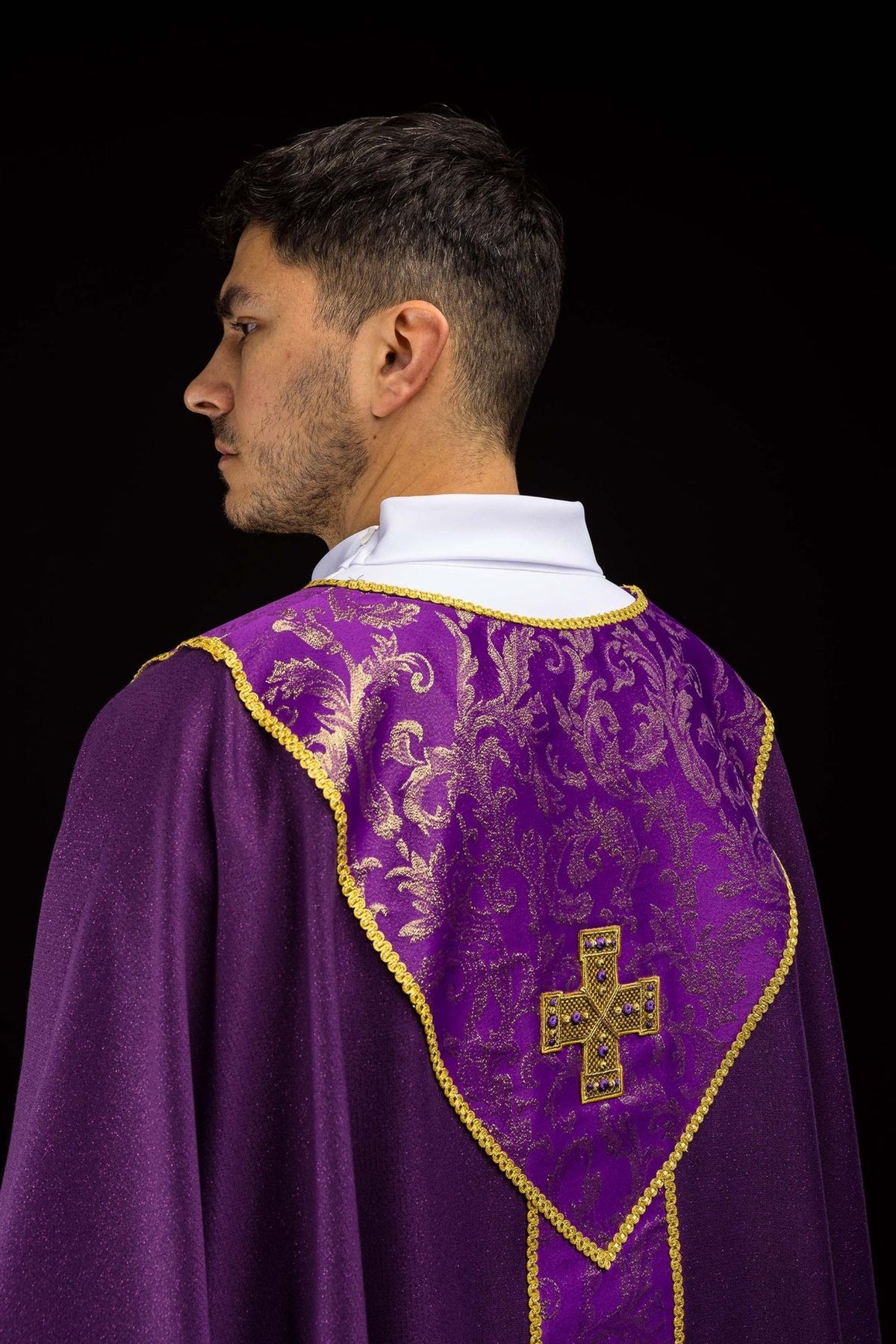 Casula litúrgica roxa vista pelas costas, com cruz dourada e faixa jacquard