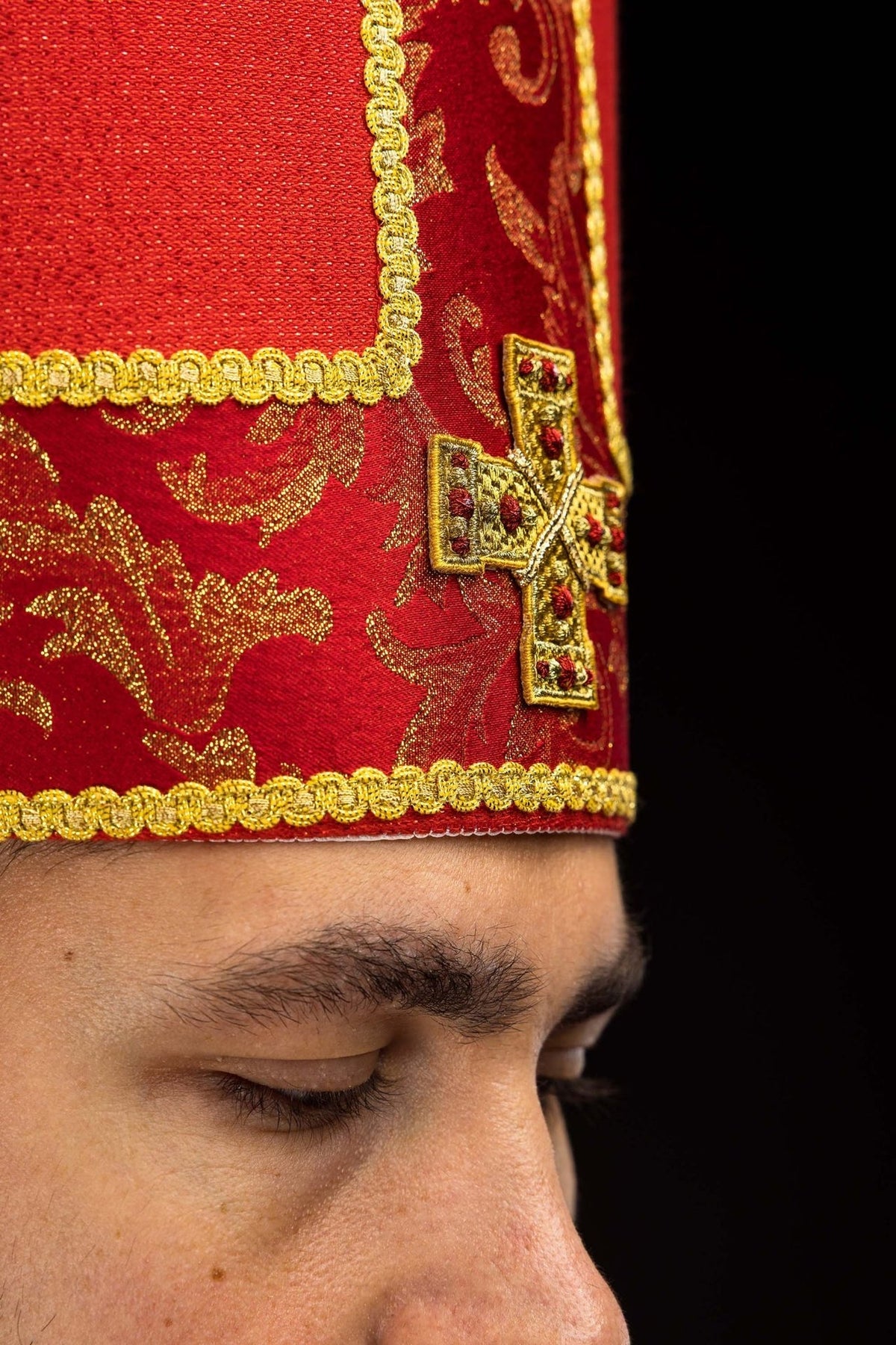 Mitra litúrgica vermelha, detalhe lateral da cruz bordada e do viés dourado