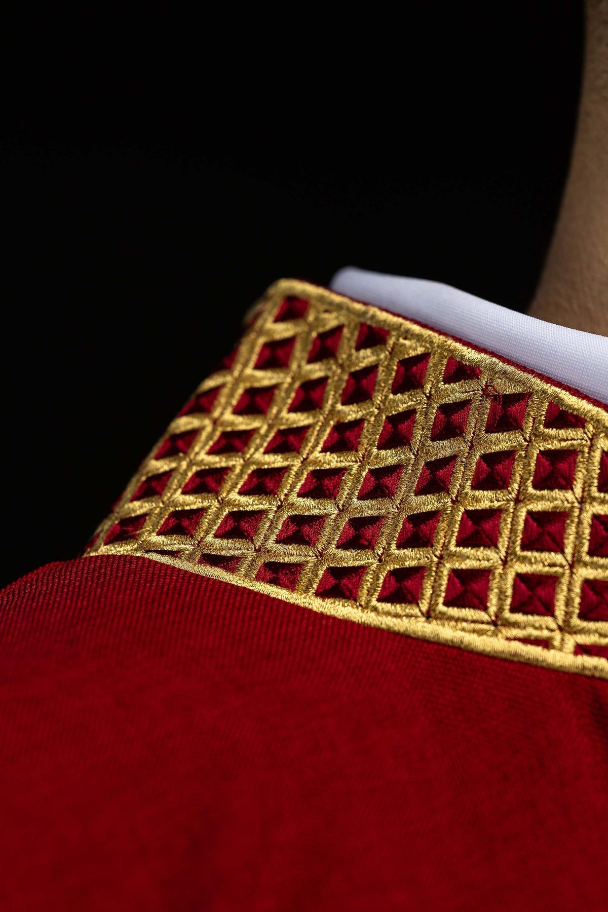 Dalmática vermelha em close-up da gola bordada com padrão geométrico dourado