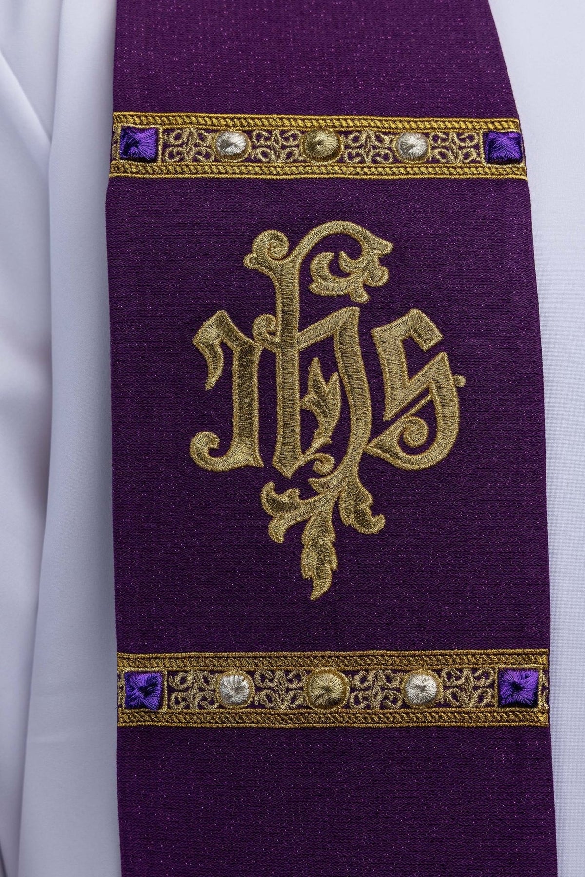 Estola sacerdotal roxa em close-up, com monograma IHS dourado e galão bordado