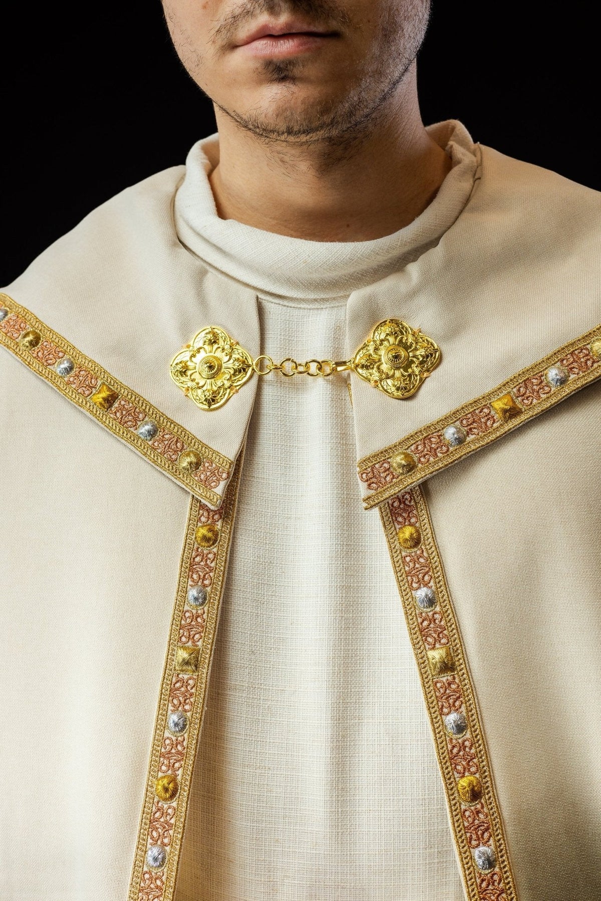 Capa de asperges creme em close-up frontal, com gola e fecho ornamentado dourado