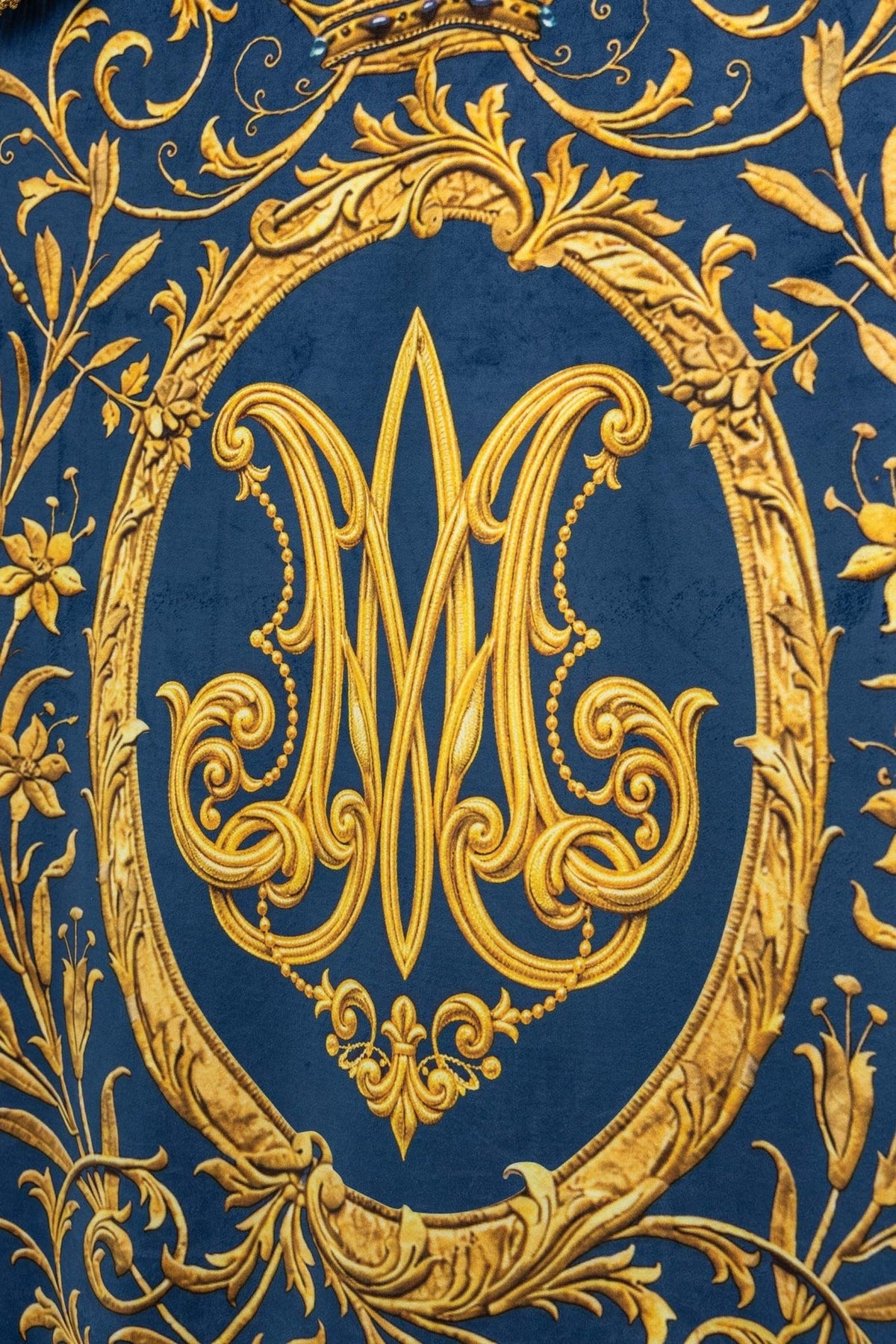 Estandarte com close-up do monograma Mariano dourado e arabescos sobre fundo azul