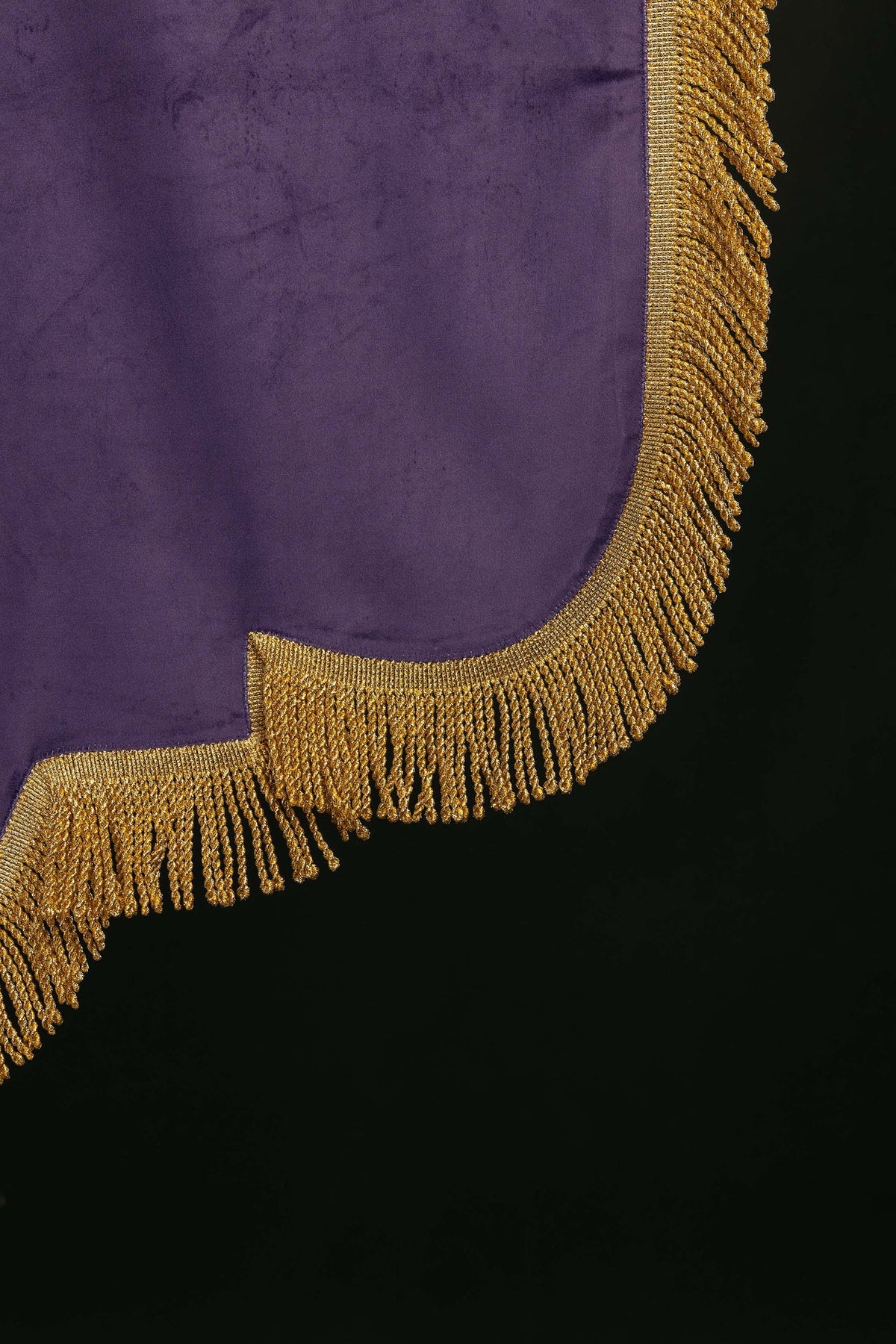 Estandarte roxo, close-up da franja dourada no canto inferior e acabamento curvo