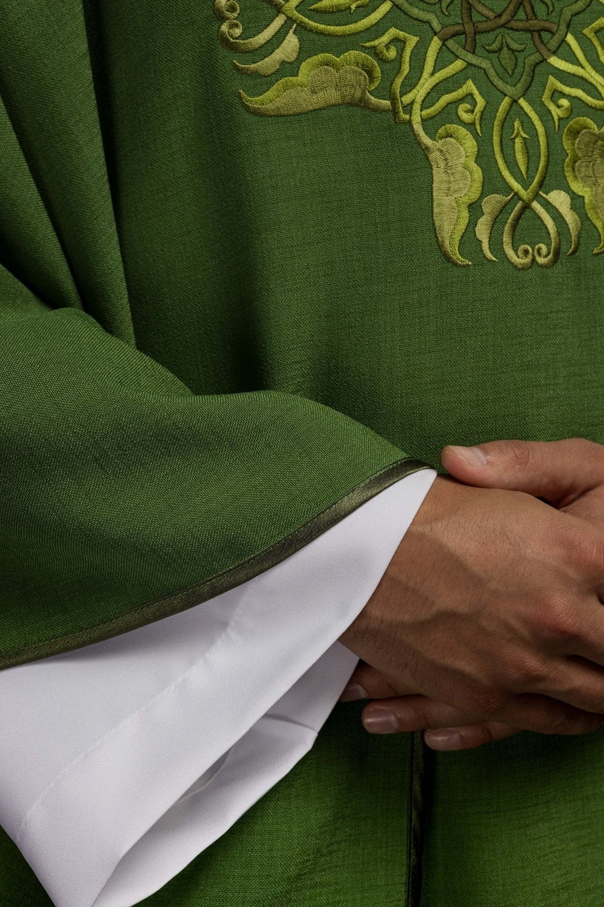 Casula verde em close-up, com bordado dourado e acabamento escuro na manga